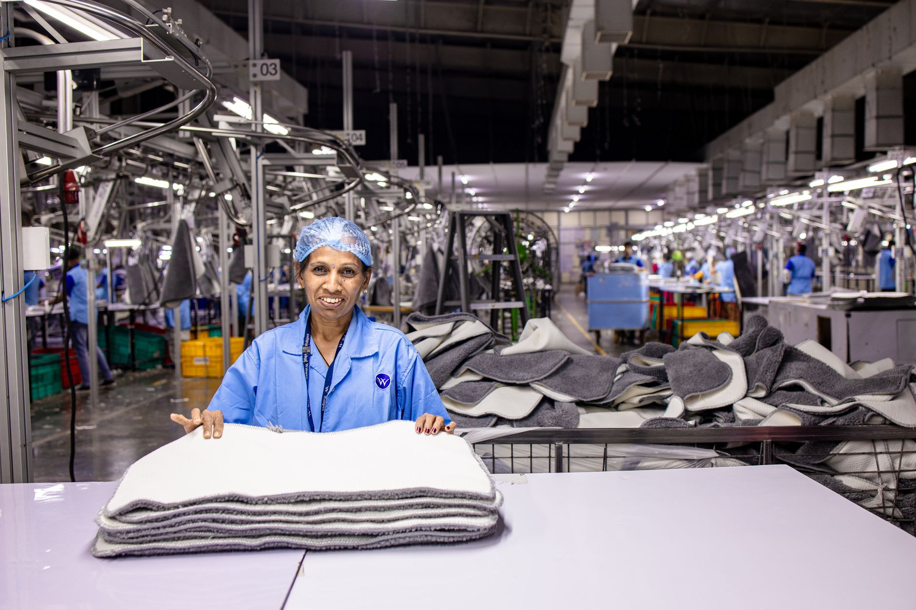 A factory worker sands a large composite panel in a dusty production workspace.