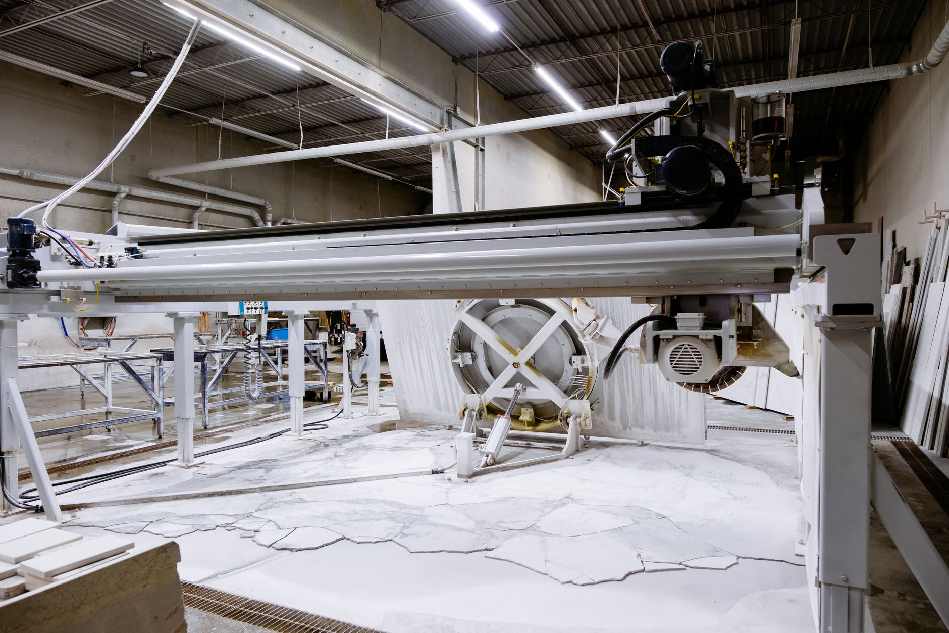 Wide view of a stone countertop fabrication shop with slabs, worktables, and cutting stations in active use.