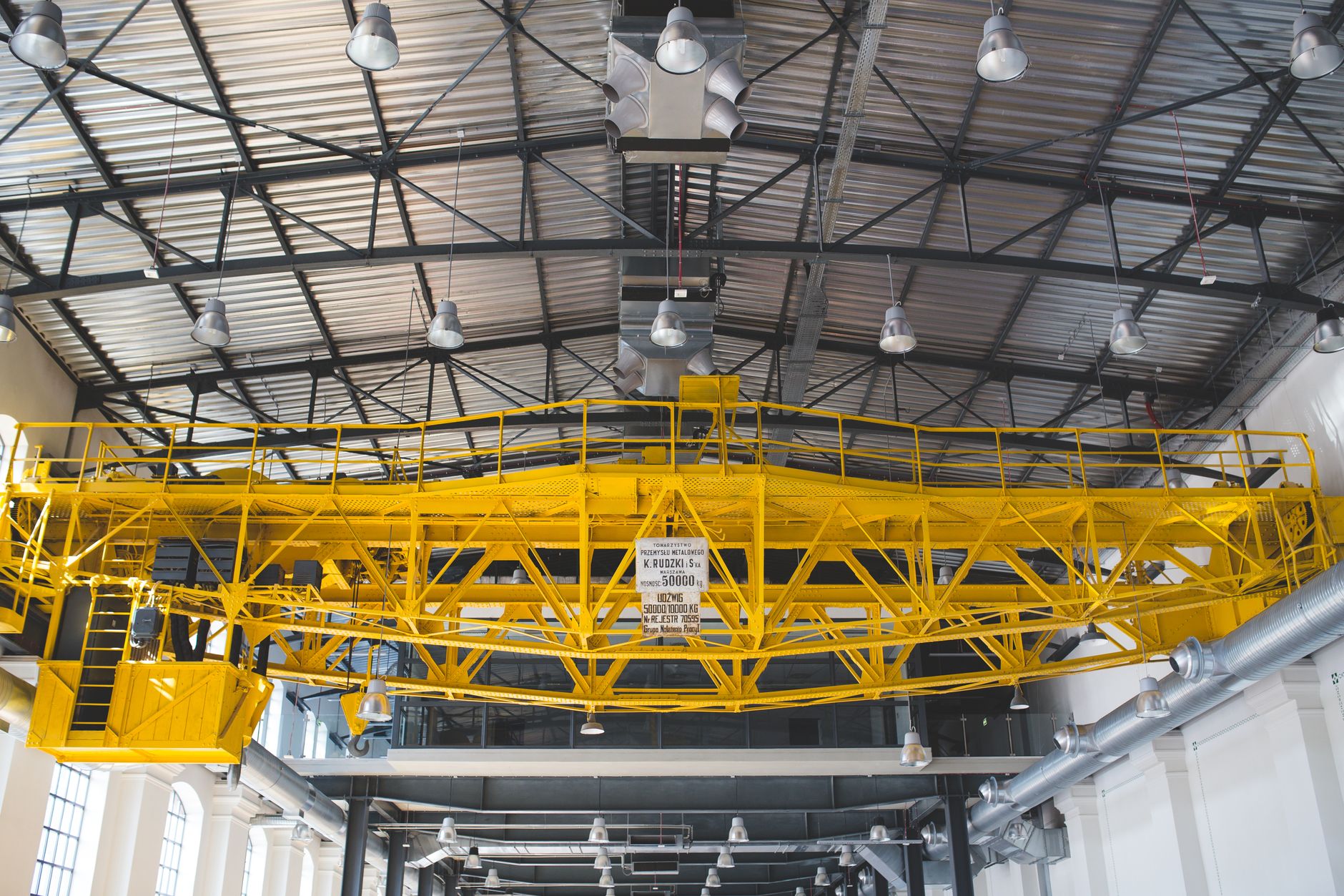 An overhead crane hook in an industrial bay where plate drops and human access must be coordinated with automated tending.