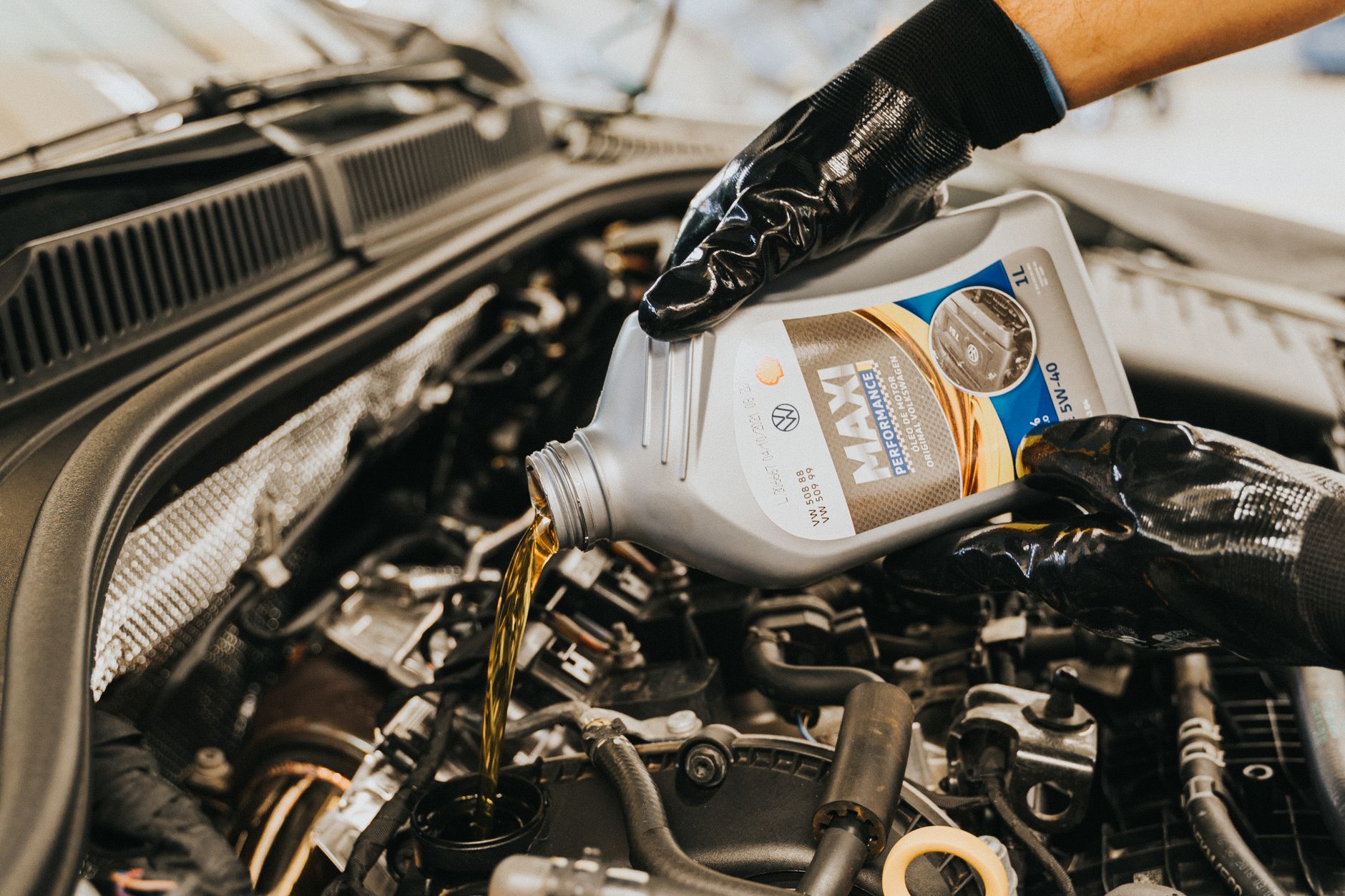 A mechanic handling motor oil during vehicle service in a busy automotive shop.