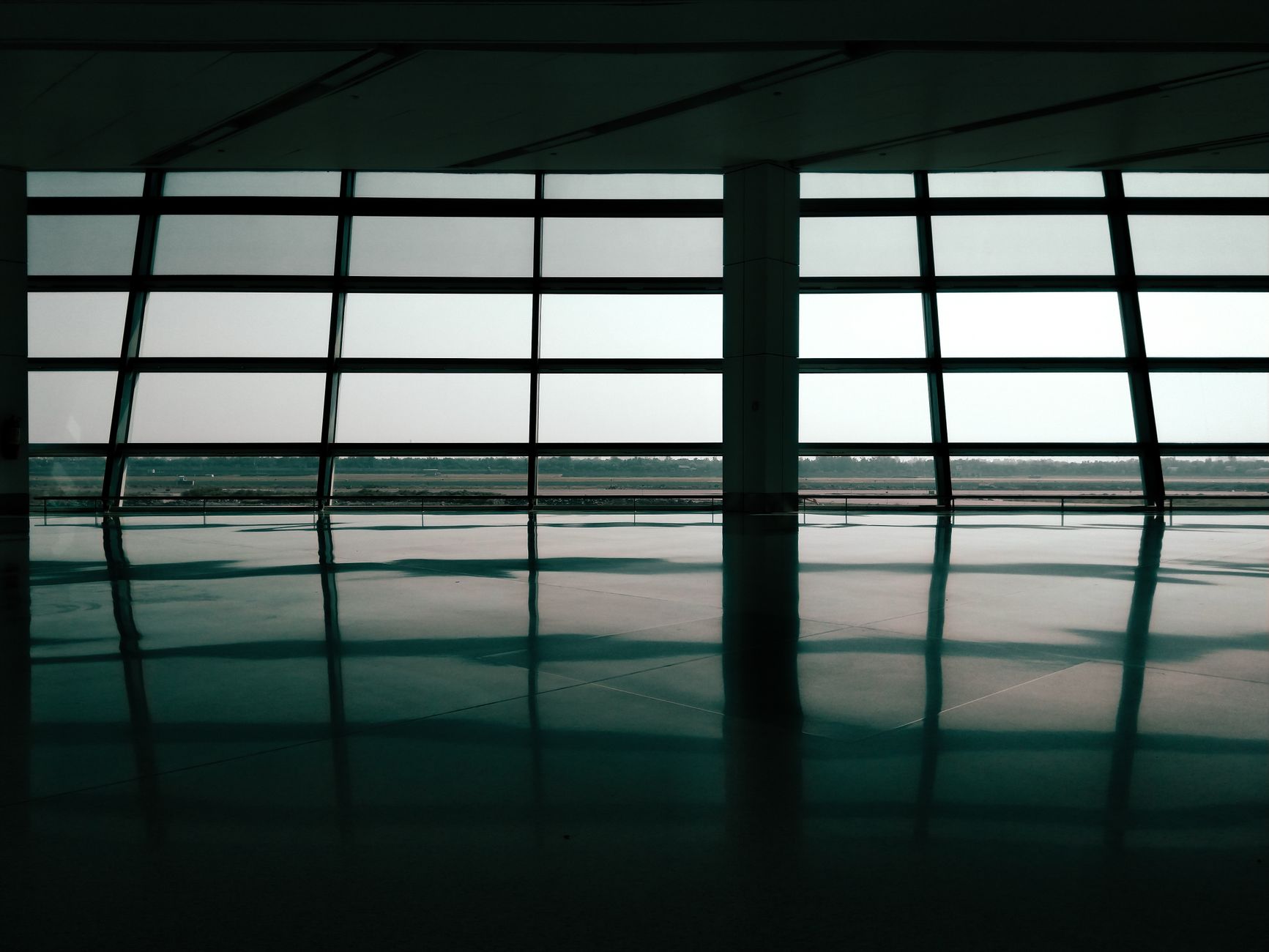 A wide, polished airport concourse floor gleams under bright lights, reflecting the ceiling and distant gate signs.