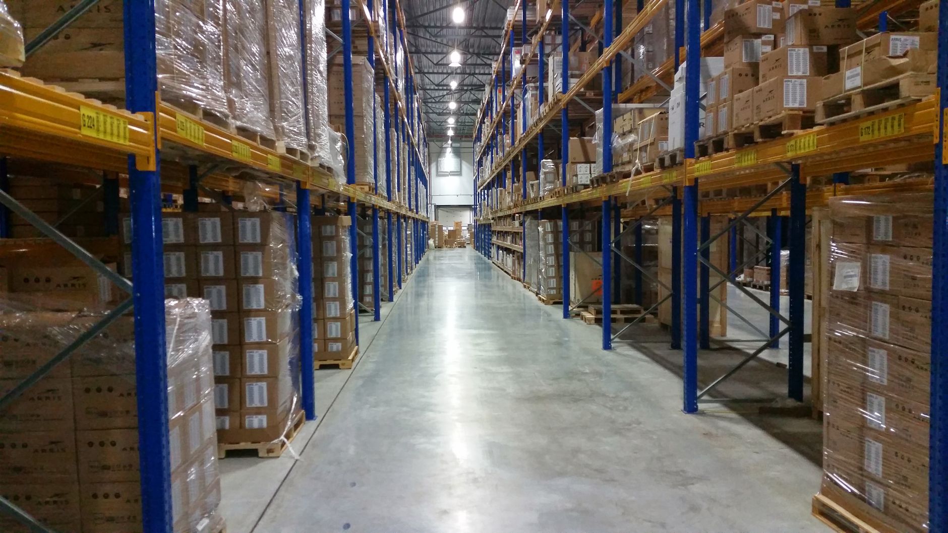 A clean, well-lit warehouse aisle with neatly stacked cardboard boxes on pallets, illustrating a common environment for palletizing and packing tasks.