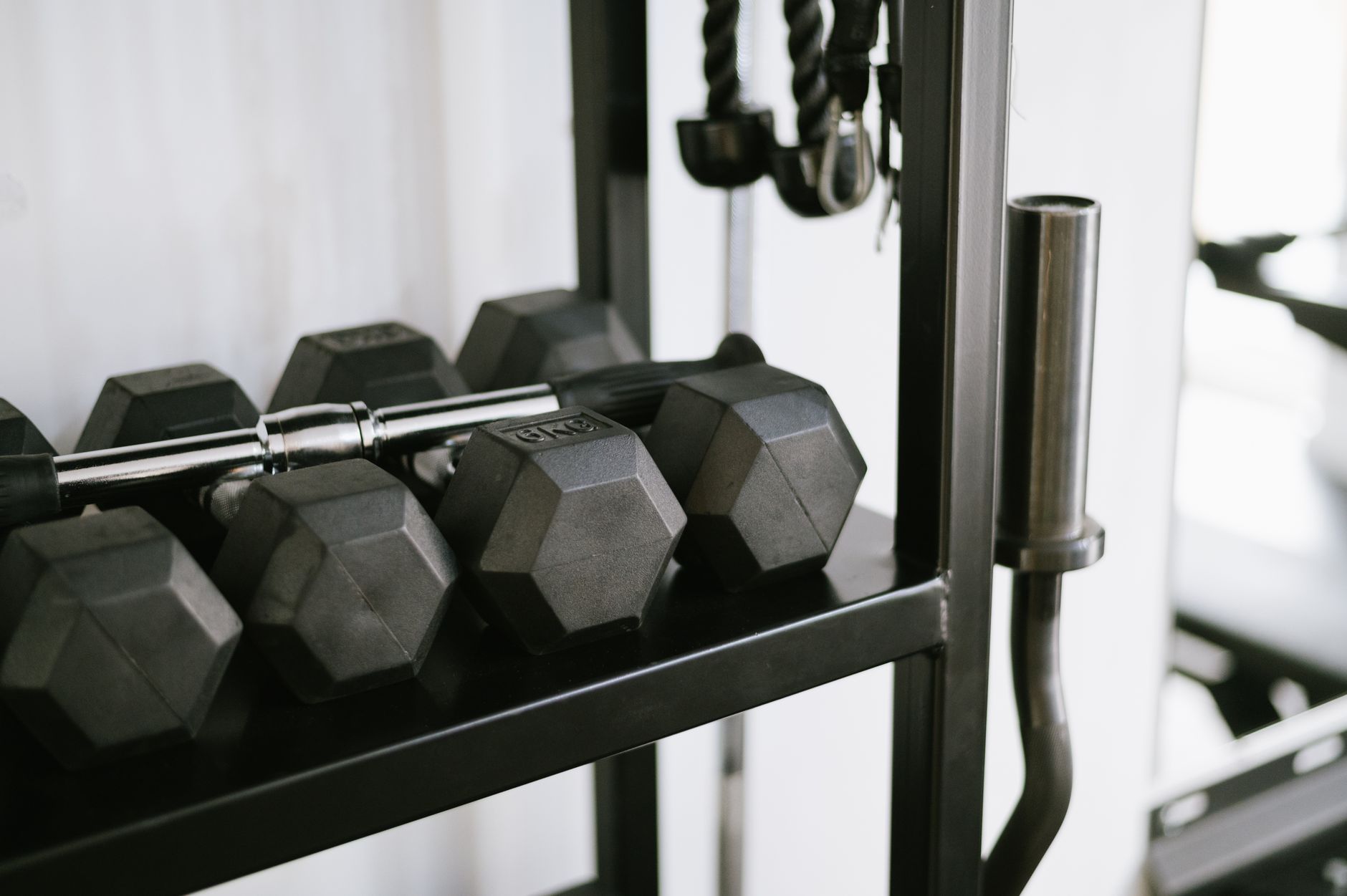 Person wiping down a gym bench and equipment handles with a cloth and cleaning product.