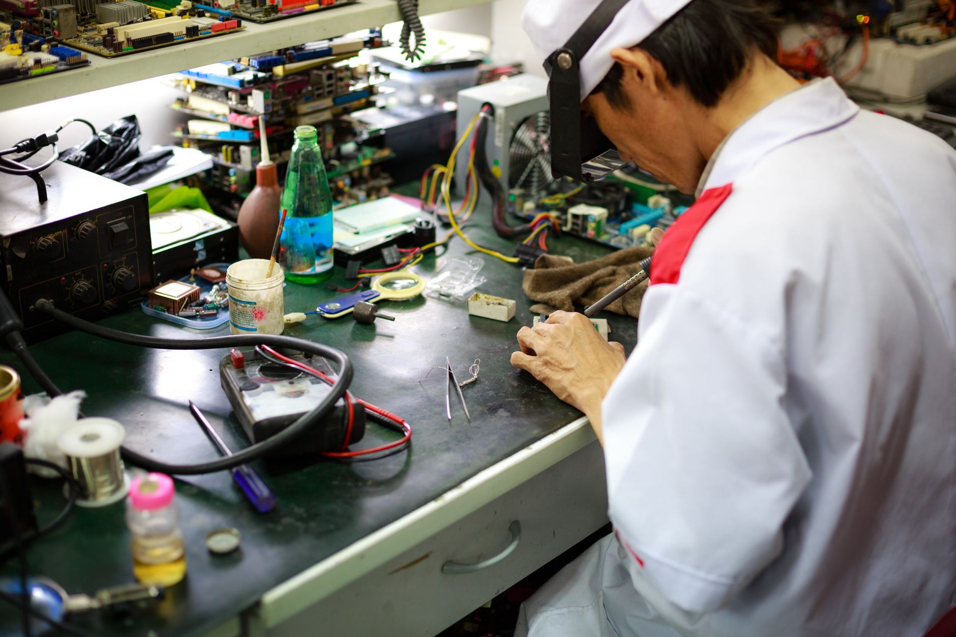 Electronics technician working at a dense rework bench with boards, tools, and fixtures in view.