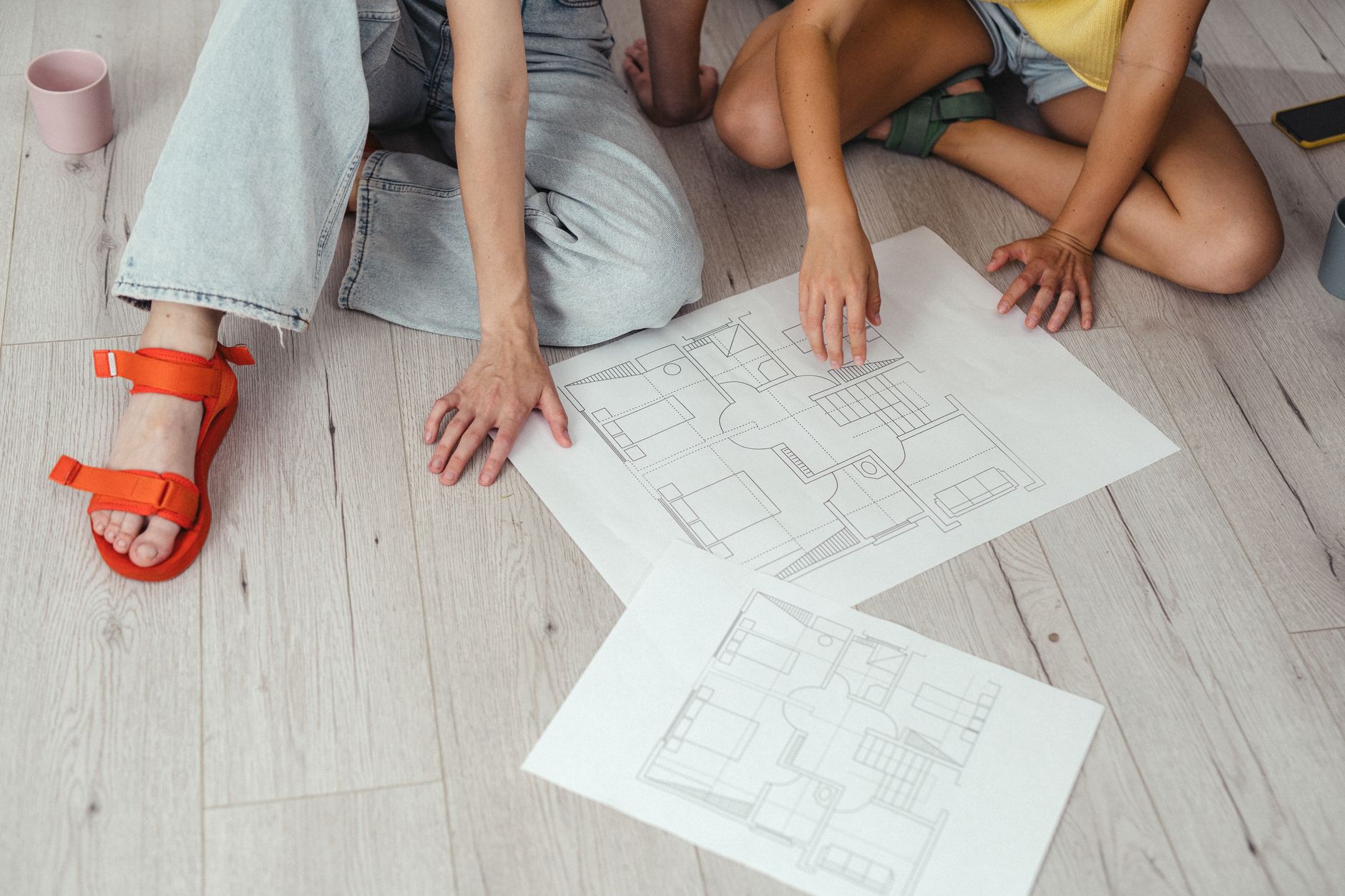 Hands reviewing a building floor plan reinforce the article’s point that map governance needs version control, approvals, and clear site-by-site oversight.