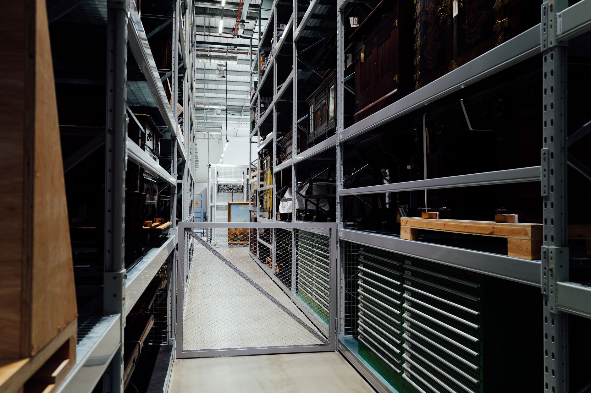 A long, orderly museum collections storage aisle with tall shelving and clear walking space, illustrating the controlled back-of-house environment where internal transport happens.
