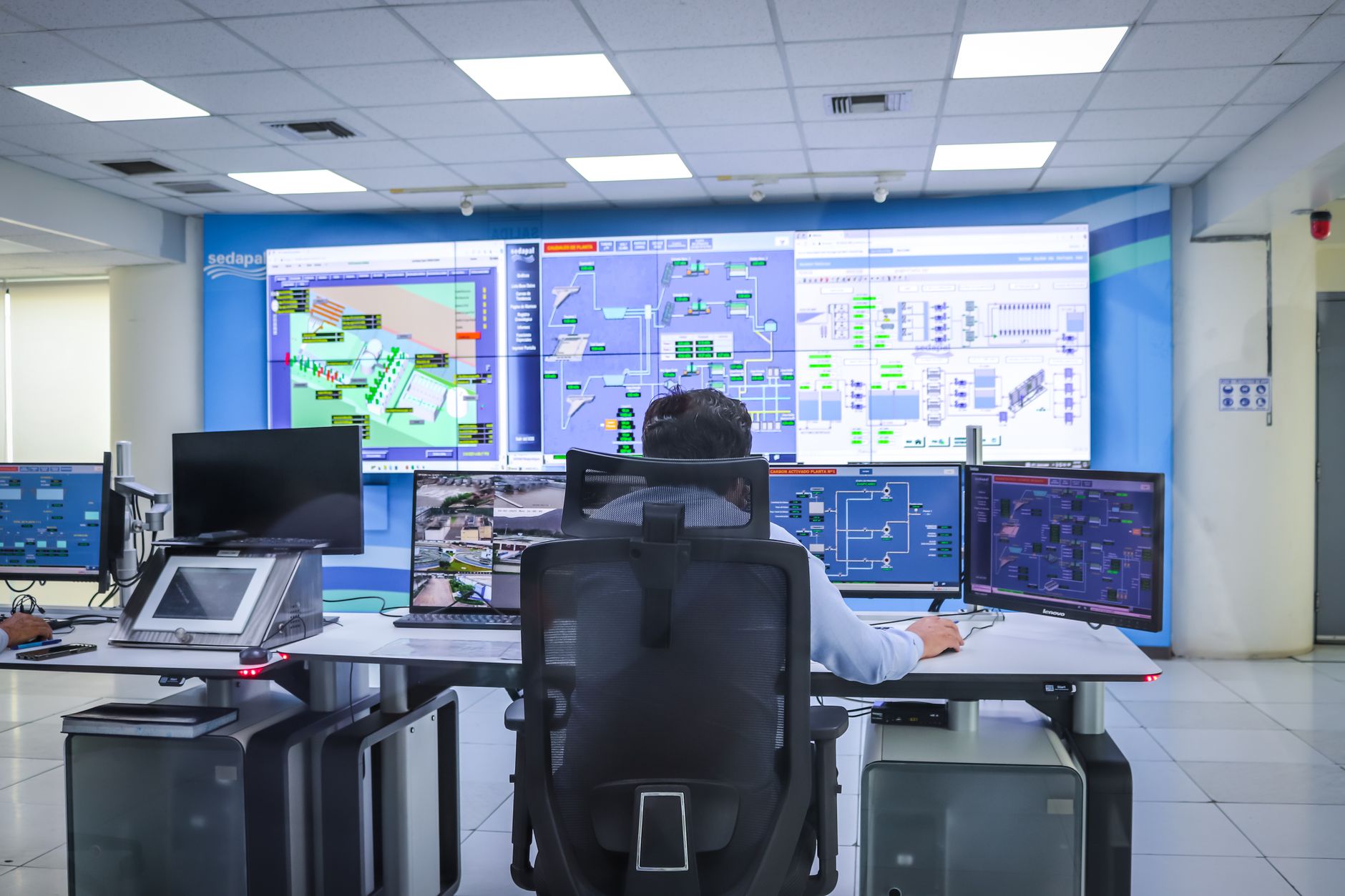 A professional remote robot operator monitors a bank of screens showing data and video feeds in a modern command center.
