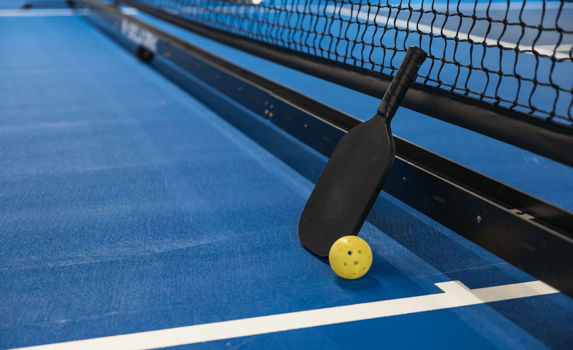 Wide view of an indoor pickleball club with multiple clean courts, fence lines, and sideline seating before players arrive.