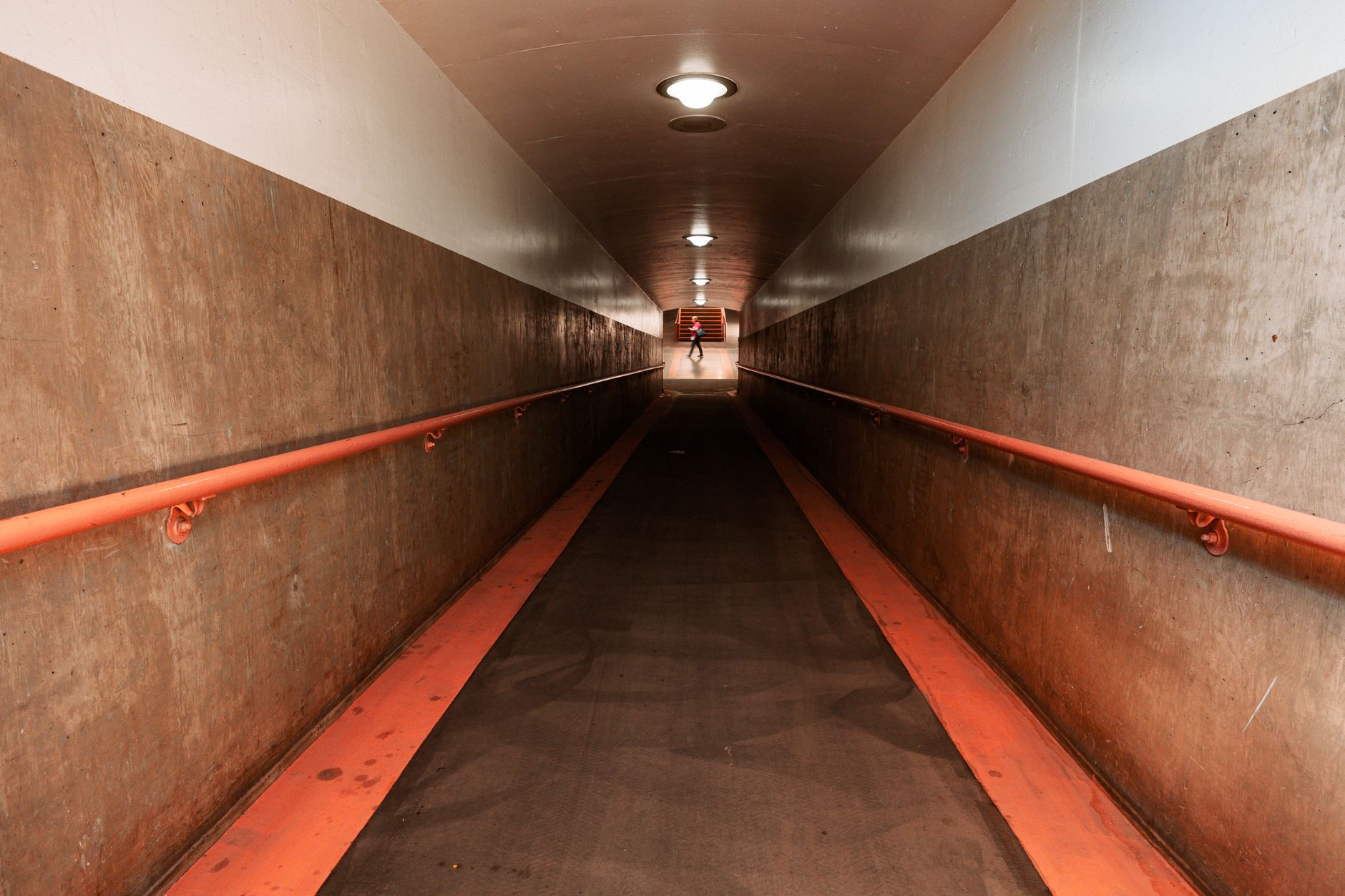 Long underground service corridor with exposed piping and limited visibility, illustrating why routine tunnel rounds are difficult to cover consistently.