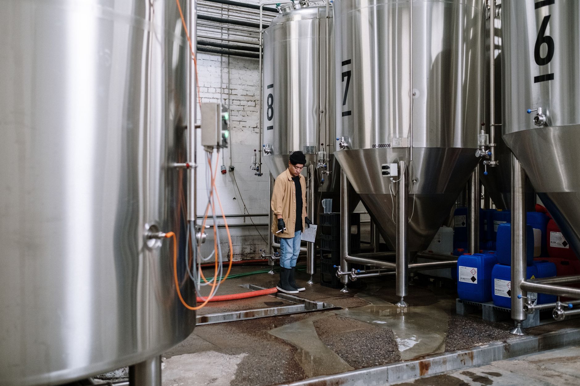 Exterior brewery tank farm with stainless process tanks, service walkways, and utility piping where inspection routes often happen outside the packaging hall.