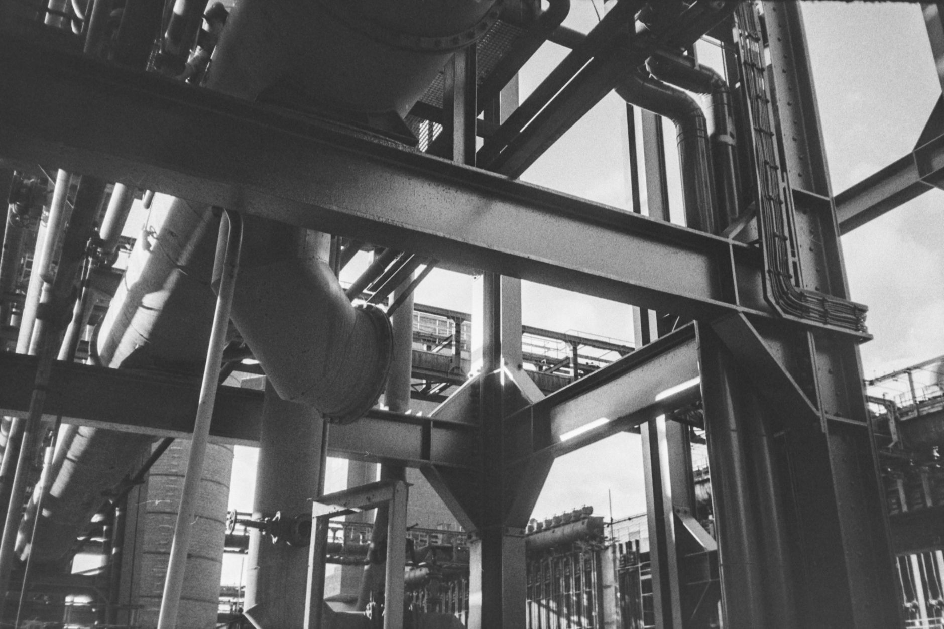 Dense pipe rack along a factory aisle where acoustic sensors listen for leak hiss.