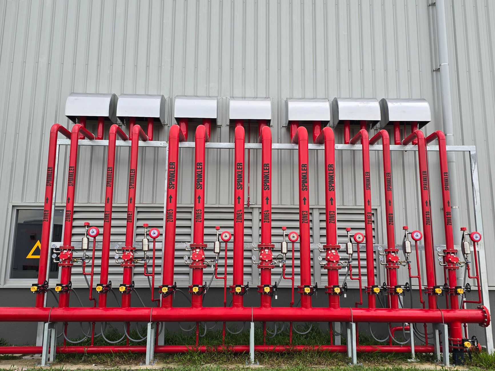 A fire sprinkler riser room with red piping, control valves, pressure gauges, and clear floor access.