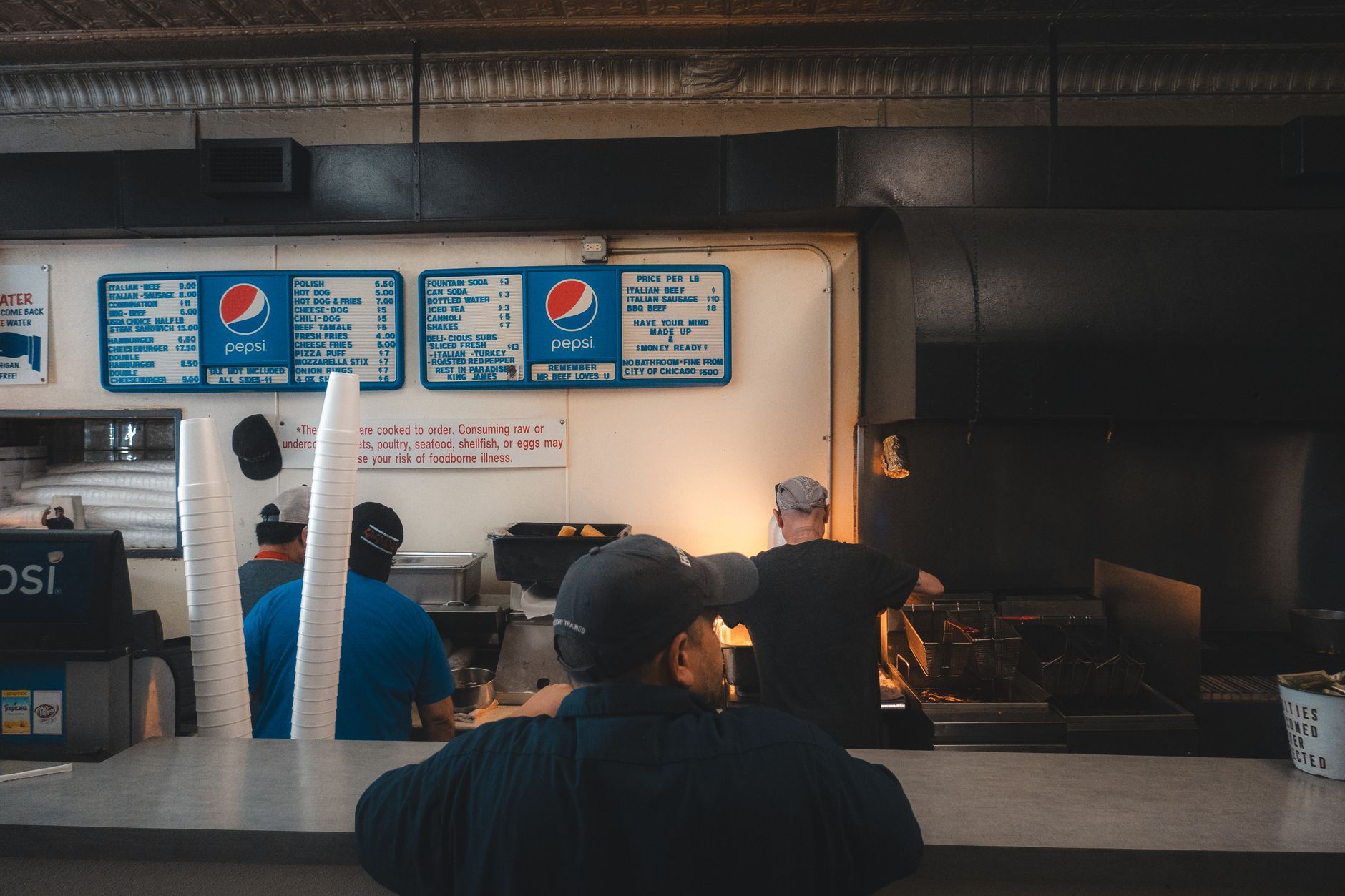 Stainless commercial kitchen hoods and ductwork above a busy cook line, illustrating the environment where grease-duct inspections happen.