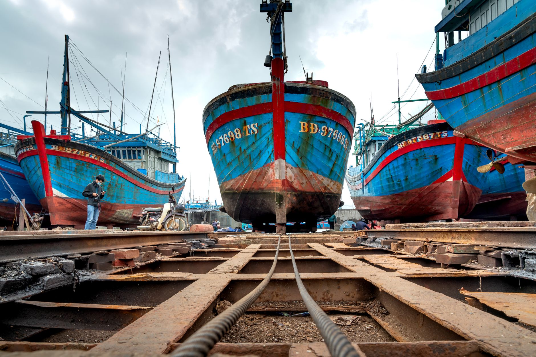 A large ship rests in dry dock while the surrounding steel structure is prepared for inspection.