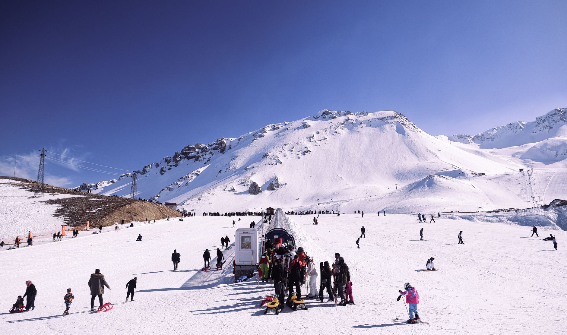 A ski lift terminal building at the base of a snowy mountain with chairs parked for the off season.