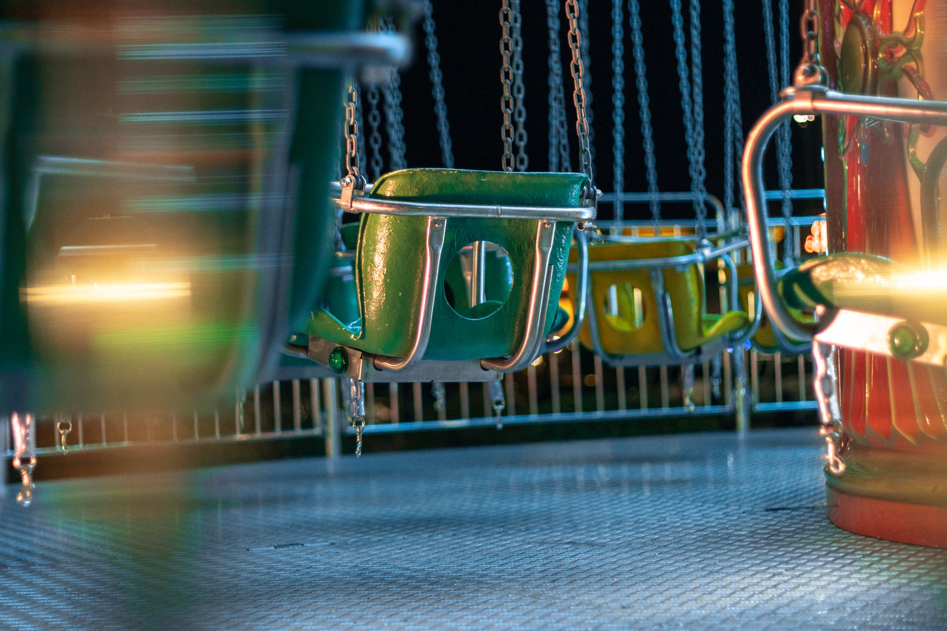An empty theme park at night, with strings of lights illuminating pristine, empty walkways and colorful, quieted rides.