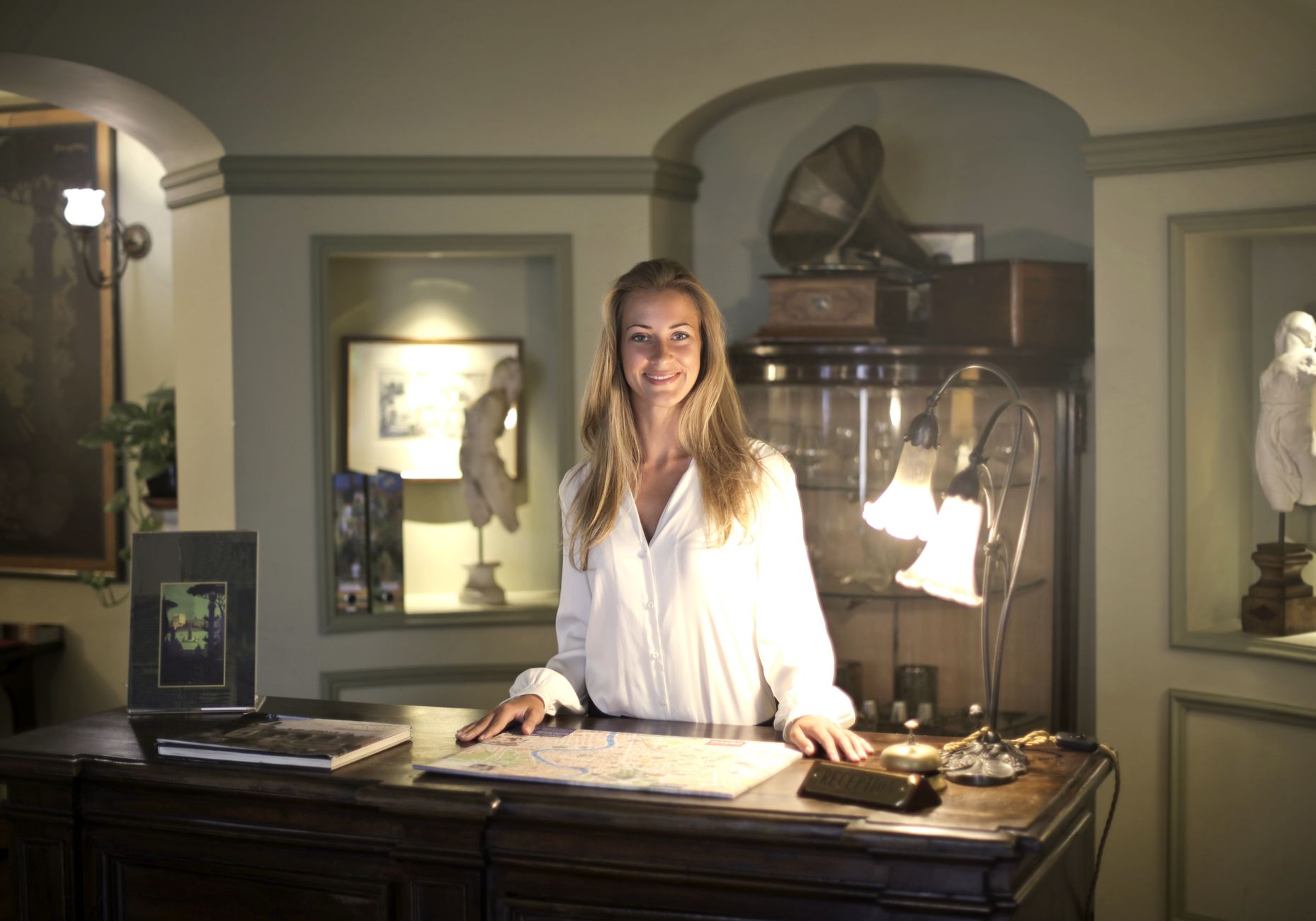 A smiling hotel staff member assists a guest at the front desk, representing the 'people payoff' of improved service.
