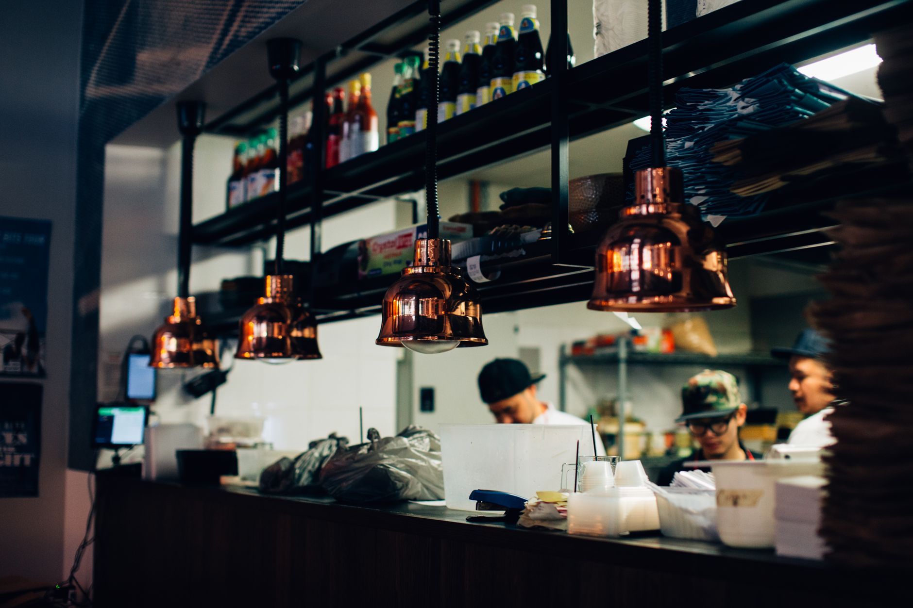 A line of chefs work over hot stoves and grills in a commercial kitchen, an environment where heat-generating equipment puts staff at high risk for heat stress.