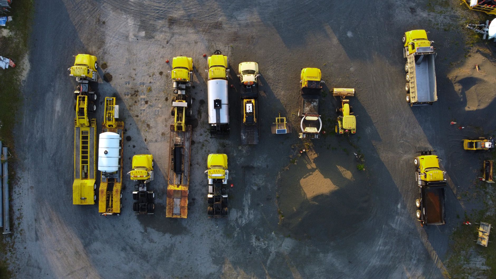 Packed gravel lanes and oil-stained aprons typical of outdoor equipment rental yards.