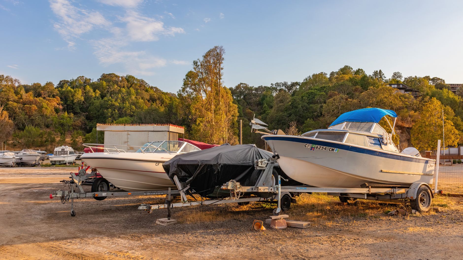 Trailers and stacked boats along a fenced storage yard