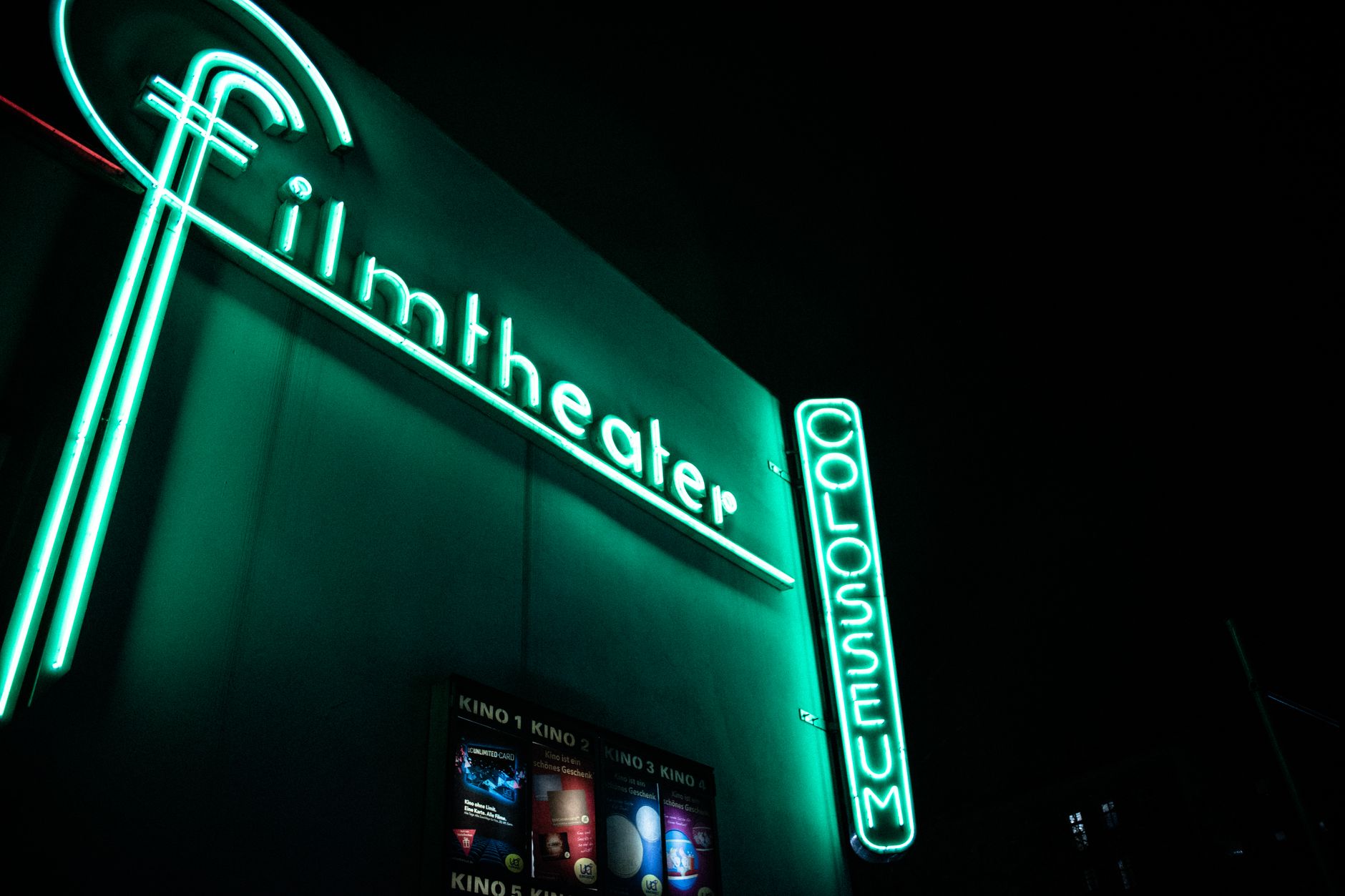 A movie theater entrance at night as guests head in, showing the pre show rush that later becomes a synchronized exit.