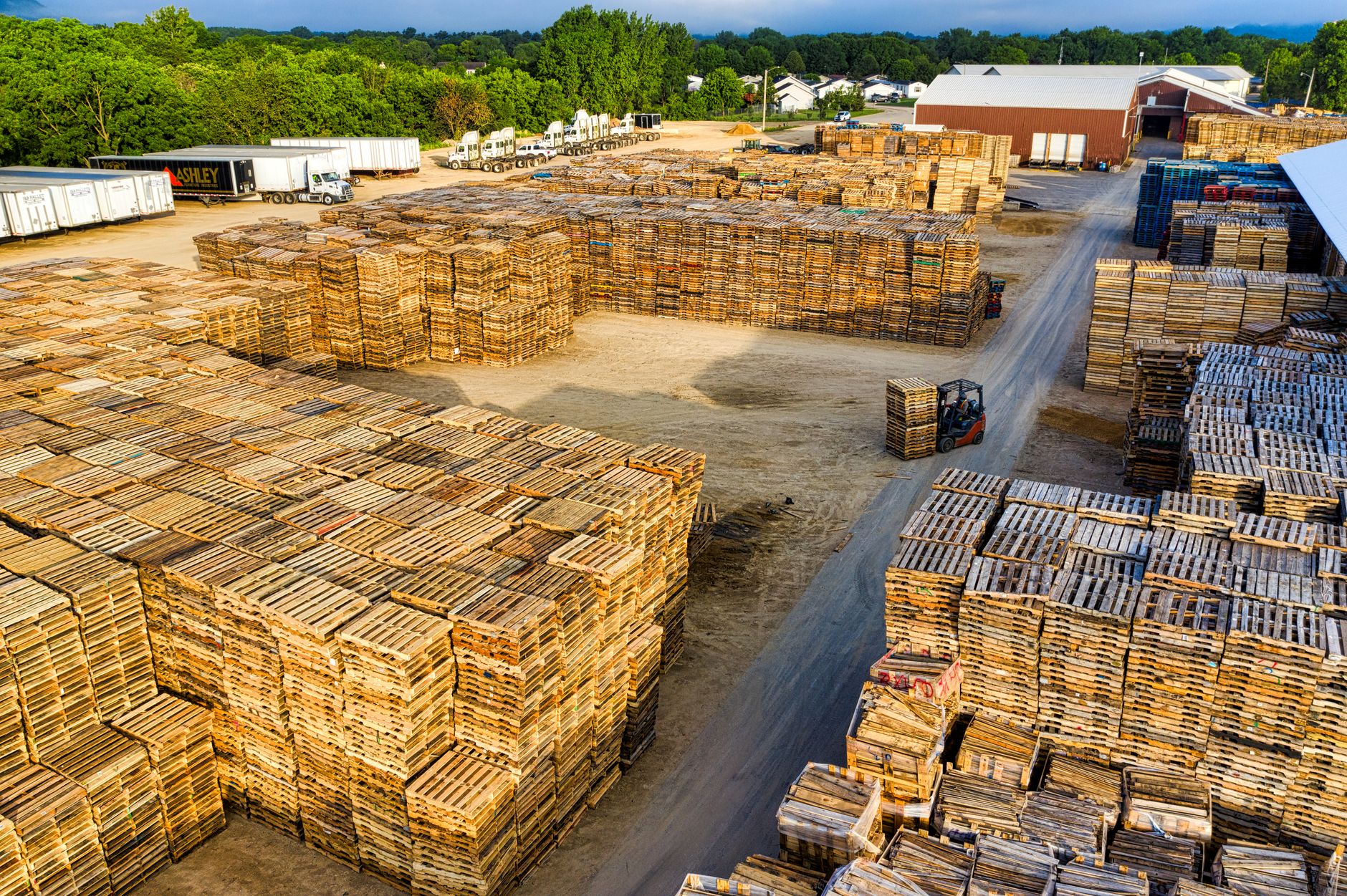 Forklift moving lumber between tall outdoor rack rows in a supply yard.