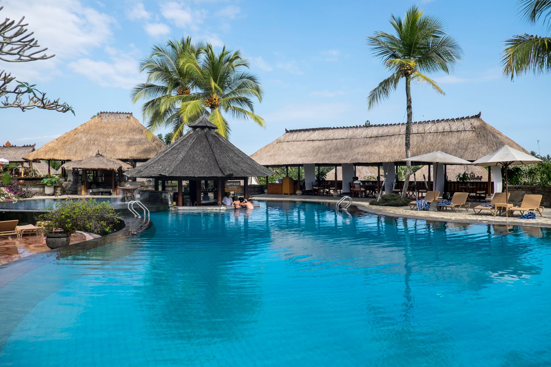 A large resort swimming pool at dawn with calm water and empty deck chairs.
