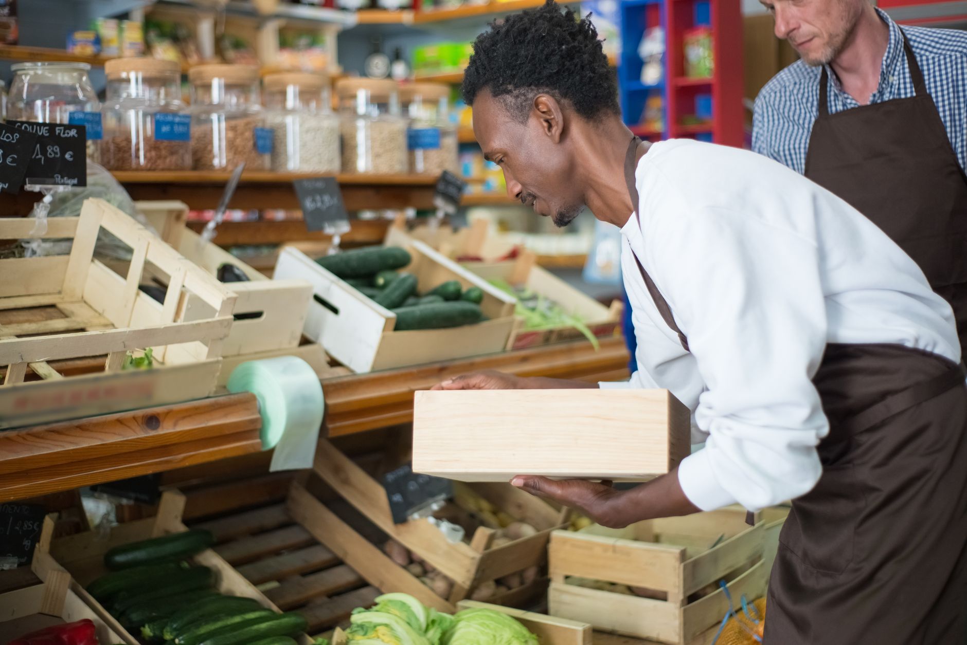 Stacked wooden crates and cardboard boxes of vegetables wait in a produce hall.