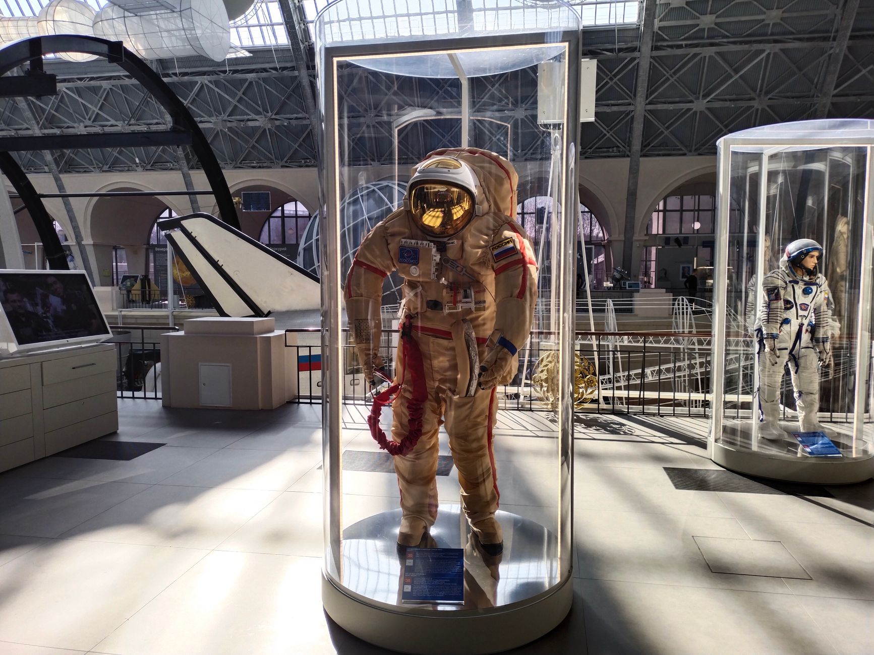 A dim museum gallery contains illuminated display cases and carefully bounded visitor paths.