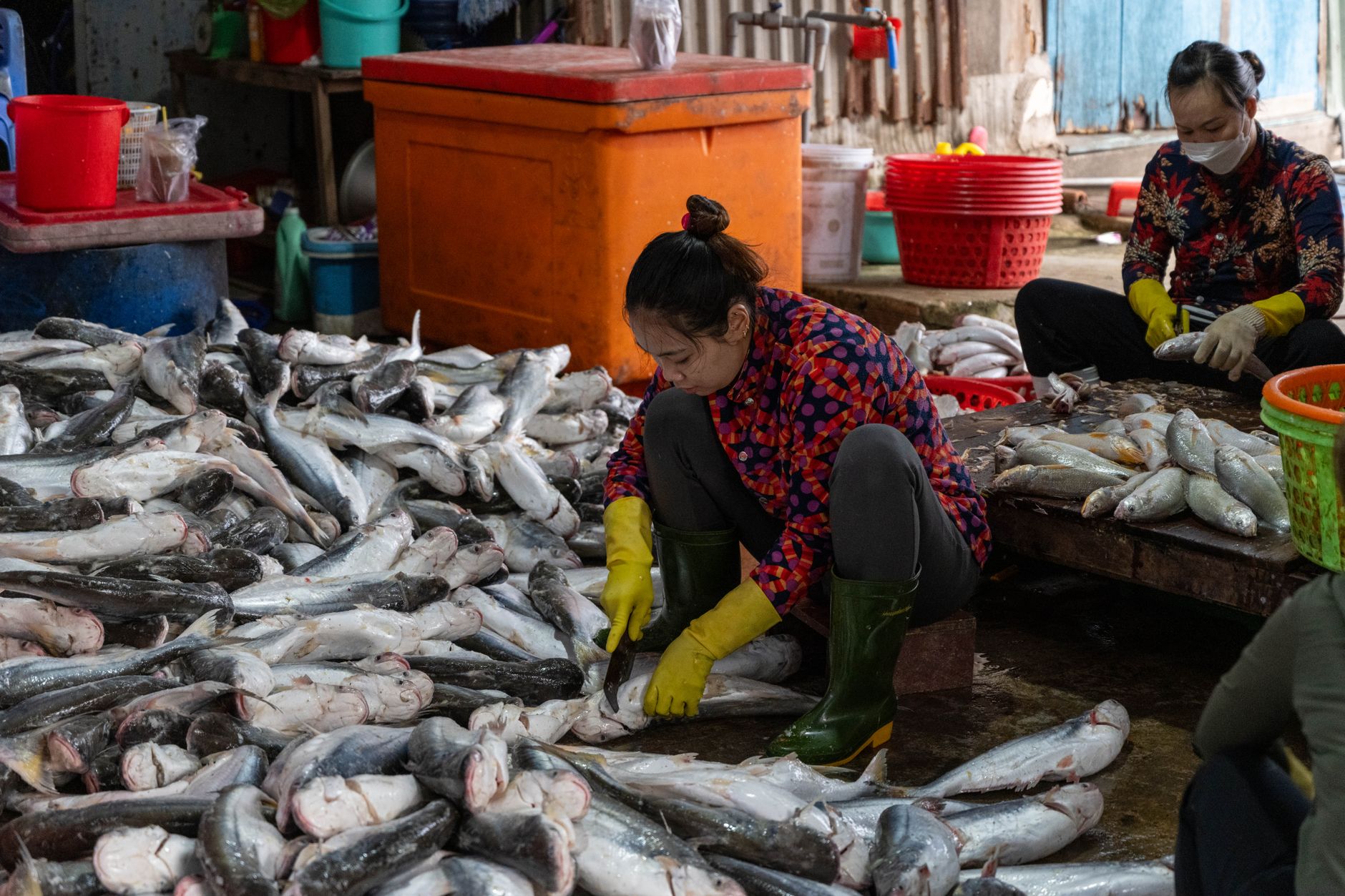 Workers move through a busy wholesale seafood market with wet floors, crates, and chilled display areas.
