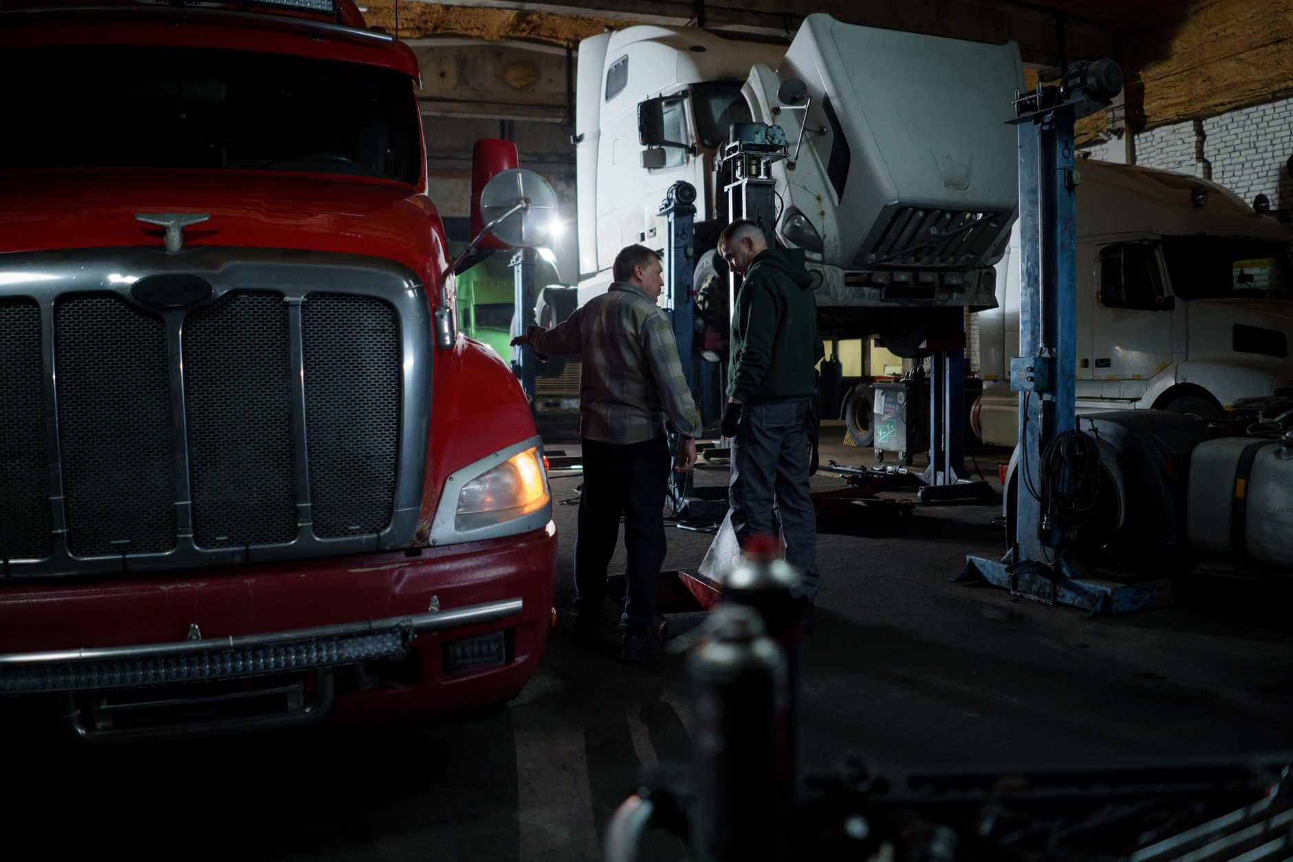 Technicians work around heavy trucks inside a commercial fleet repair bay, setting the scene for tire and wheel handling work.