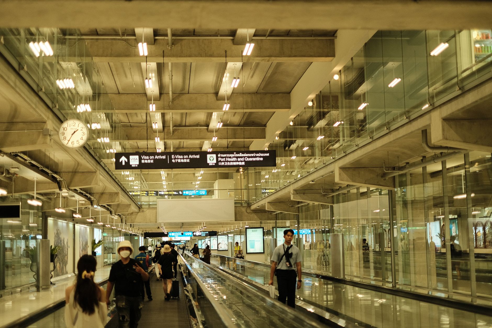 Travelers walk through a wide airport concourse with polished hard flooring