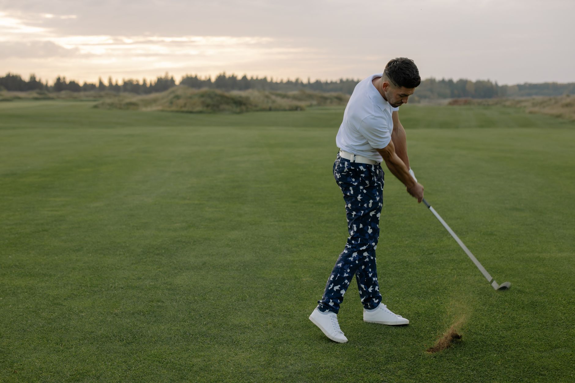 Golfers on a tee box under evening light with trees behind them.