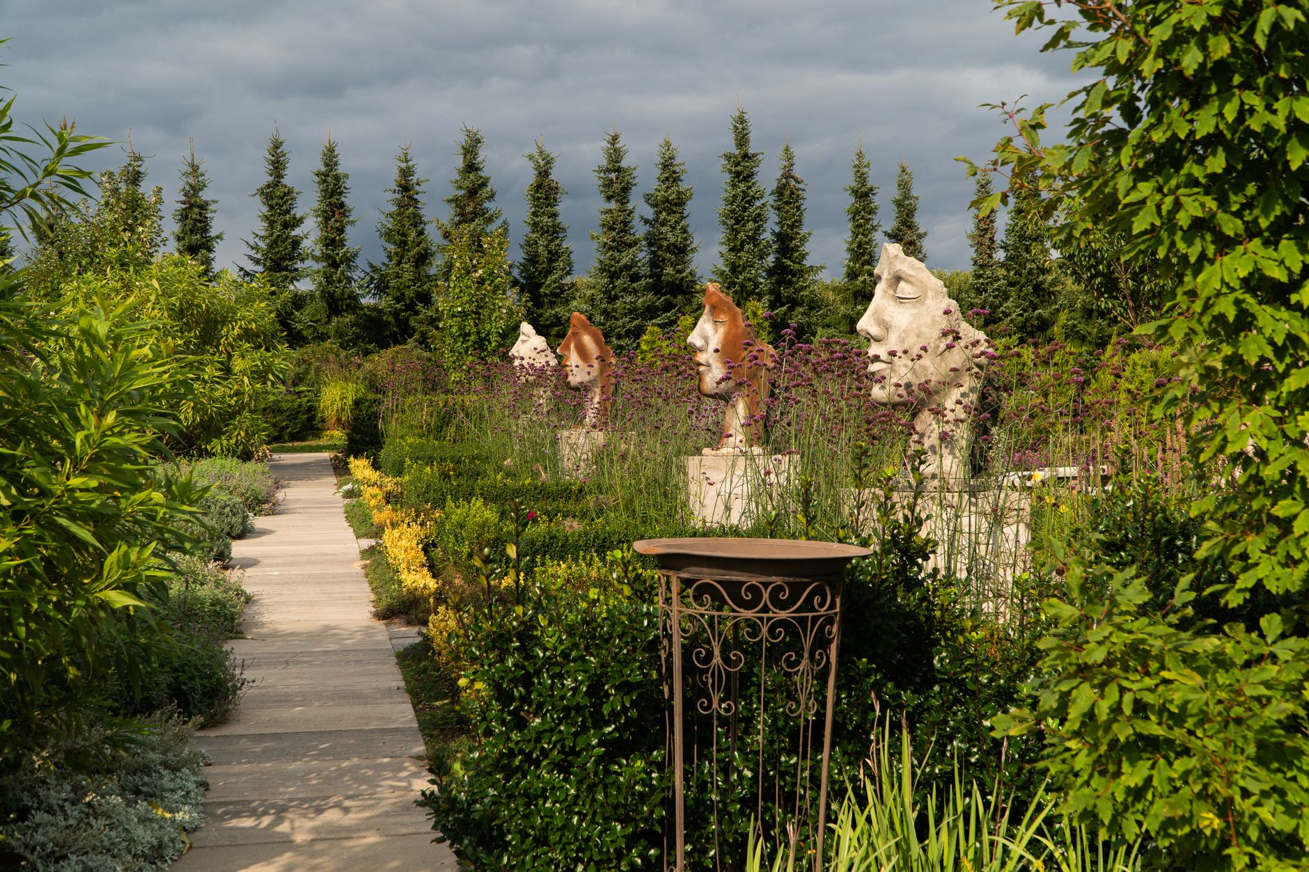 Gravel path winding through an outdoor sculpture garden with lawns and trees on a clear day.