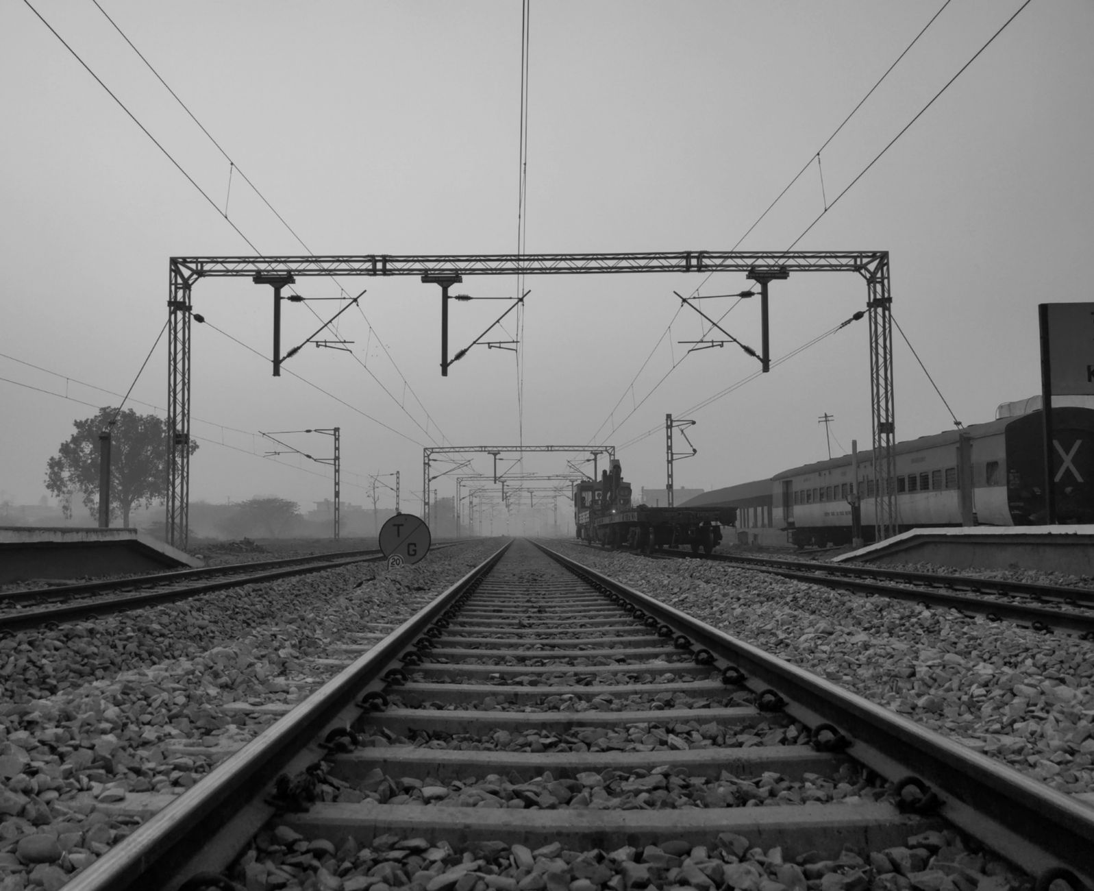 Rail tracks fade into fog beneath uneven nighttime lighting in a freight yard.