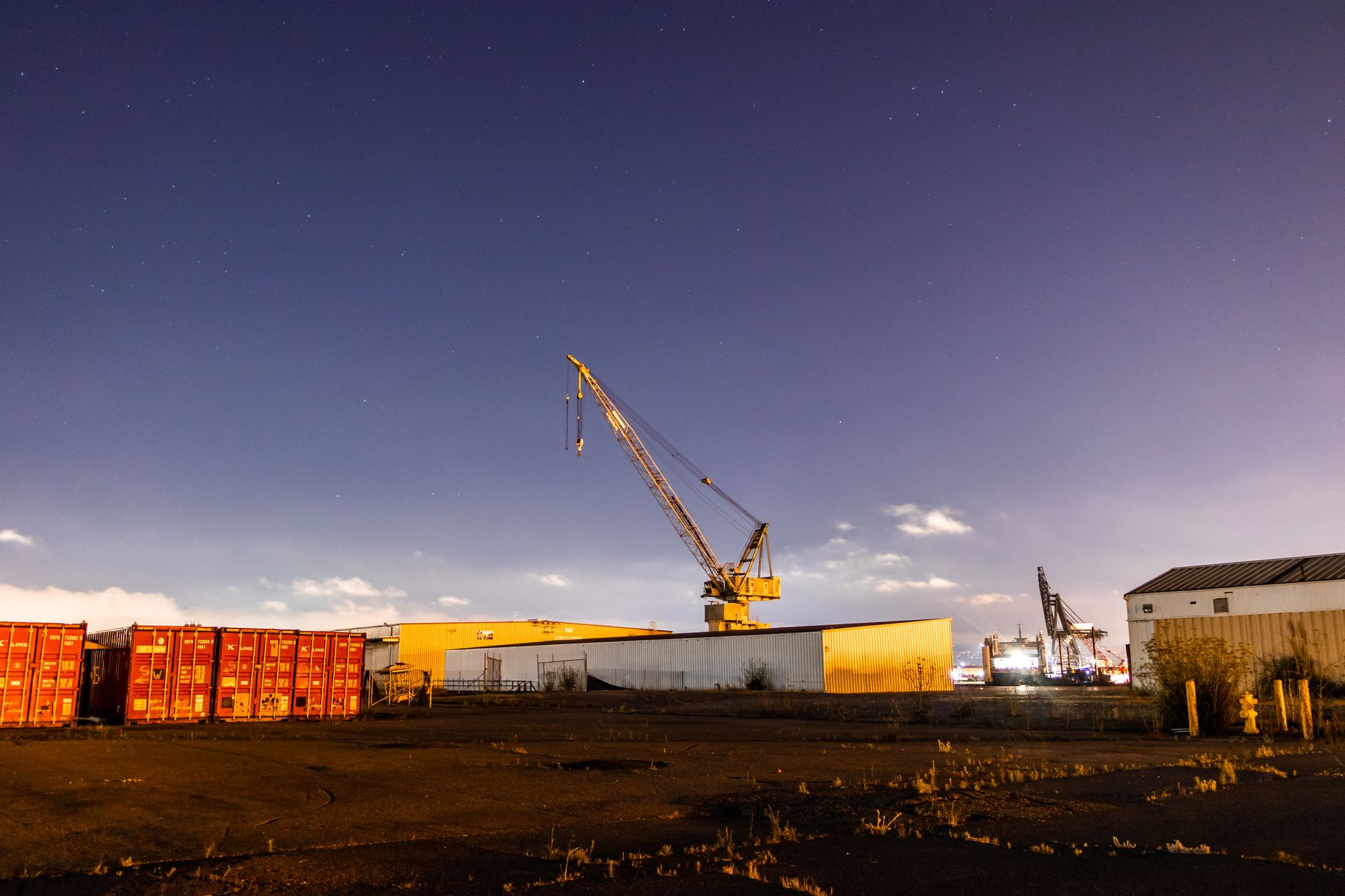 A cluttered industrial yard at night with harsh lights, shadows, and uneven ground that mirrors the surveillance challenges in a scrapyard.