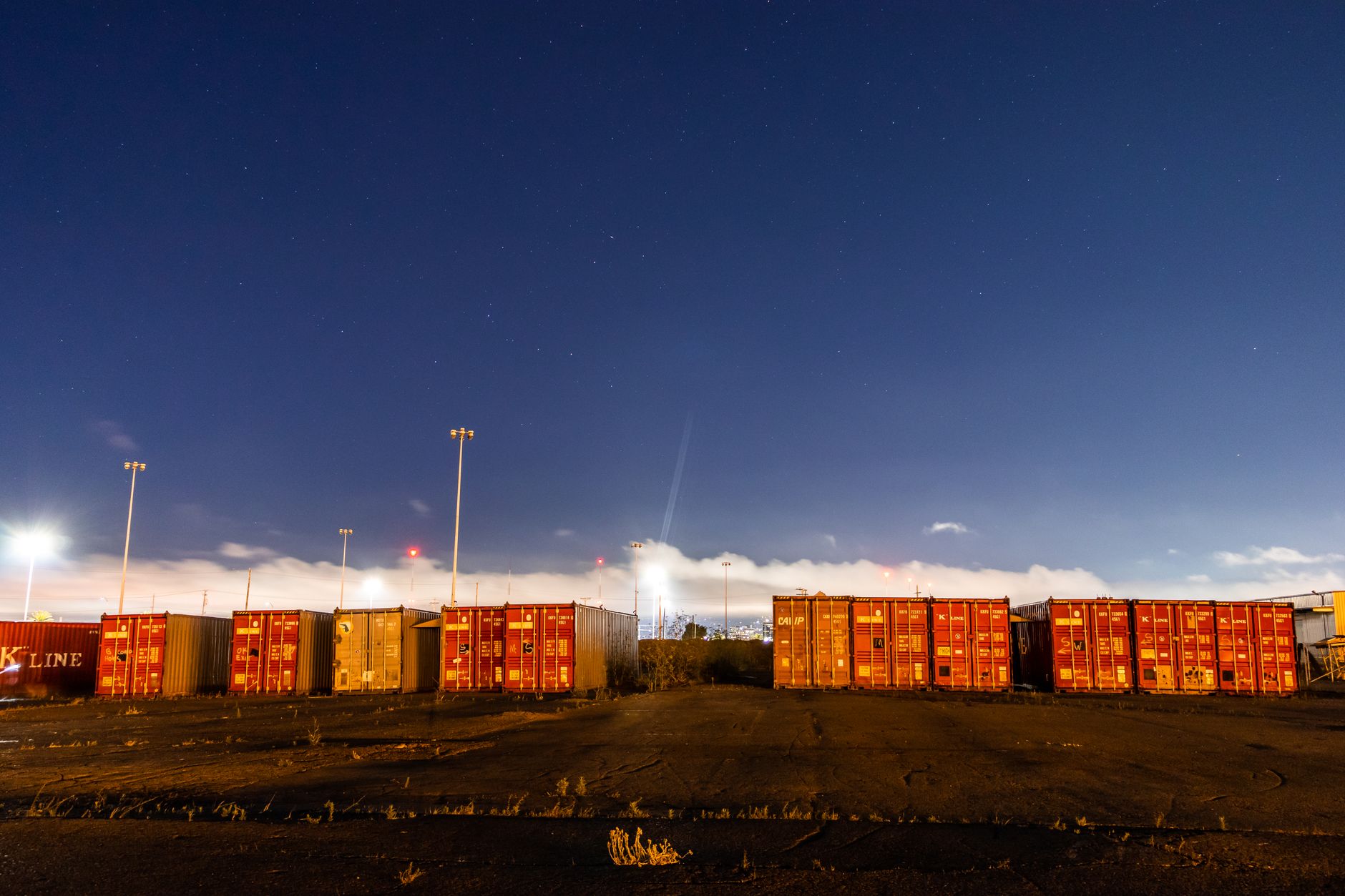 The exterior of a self-storage facility at night, with rows of garage-style doors illuminated by security lights, suggesting 24/7 surveillance.