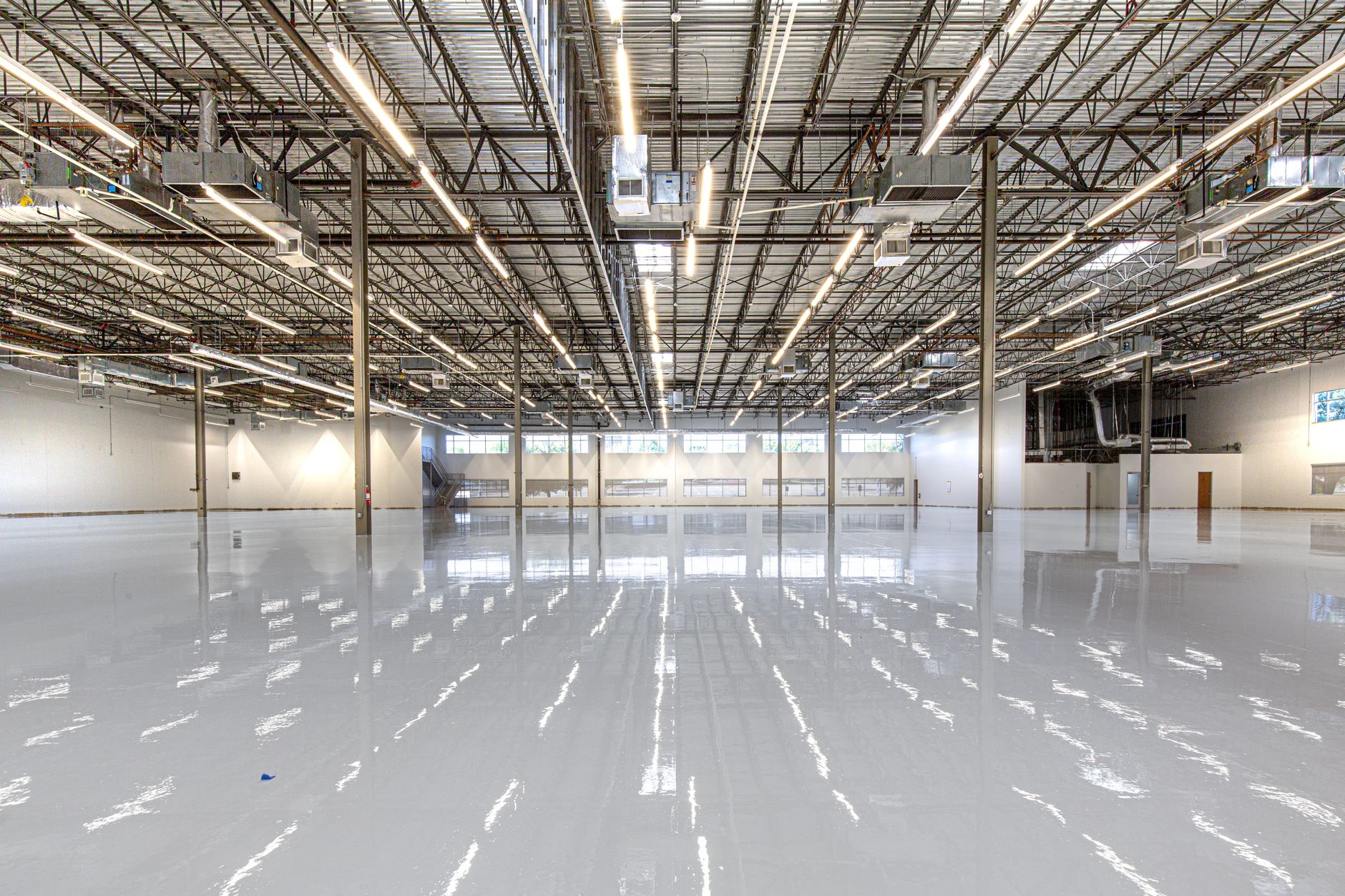 A wide-angle view of a vast, clean concrete floor in a modern warehouse, with rows of tall shelving in the distance.