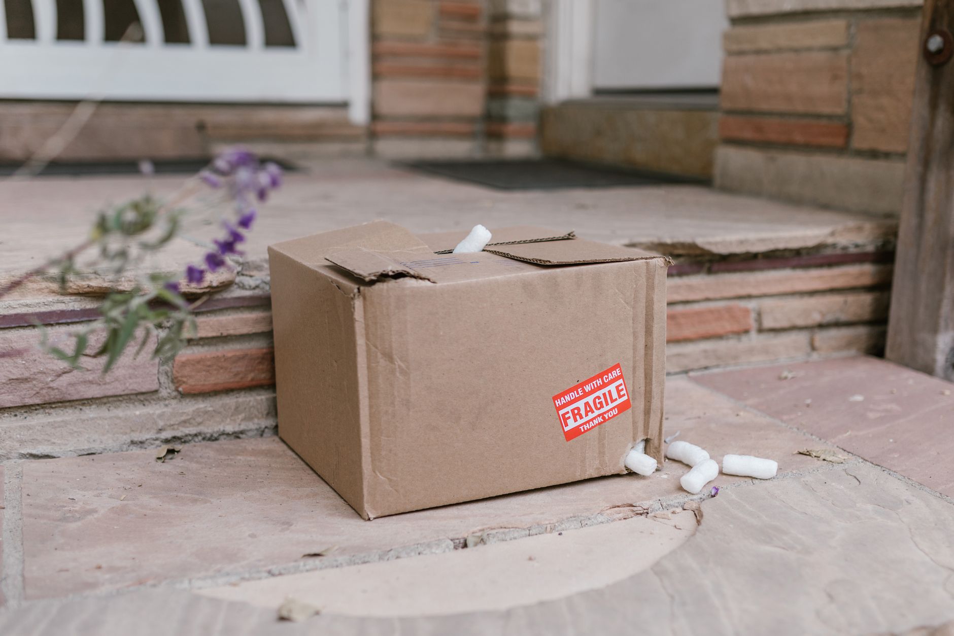 A close-up of a crushed and torn cardboard box in a warehouse, representing costly product damage.