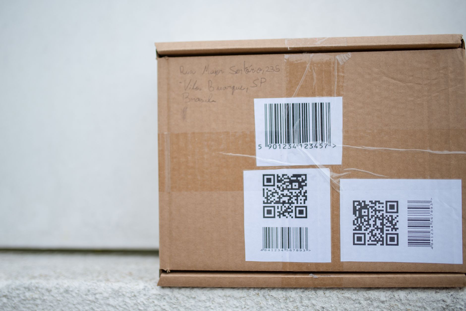 A close-up view of a barcode label on a cardboard box on a warehouse shelf, the target for an automated inventory scan.