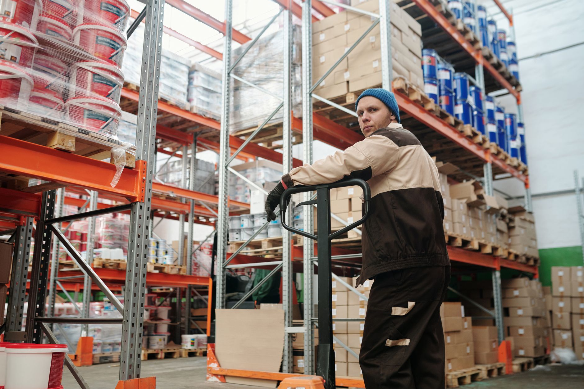 An employee stacks boxes onto a shipping pallet, a classic example of a high-risk ergonomic task involving lifting and twisting.