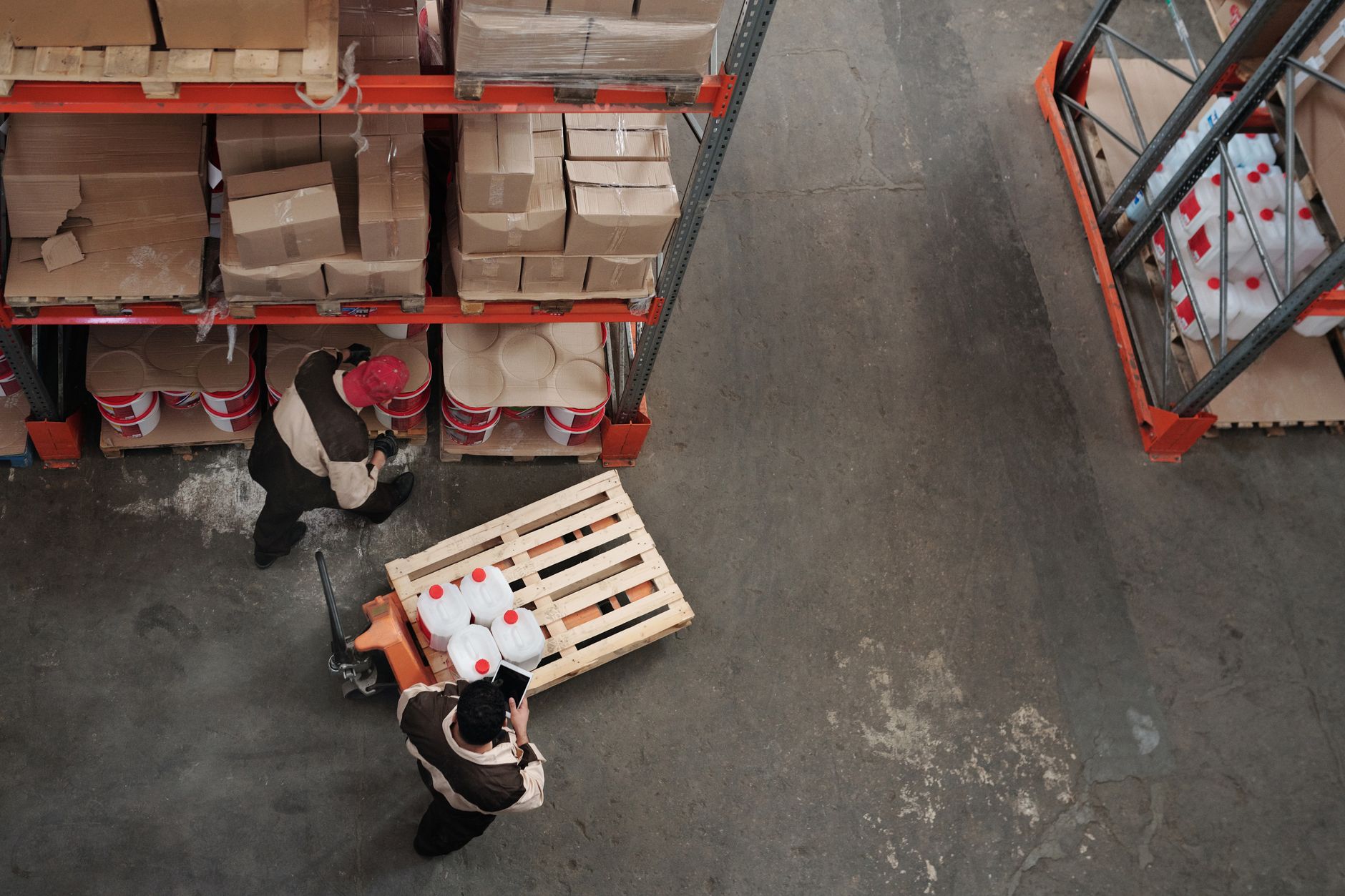 Warehouse employees move loaded carts through a wide aisle, illustrating the repetitive transport work evaluated for a first safety project.