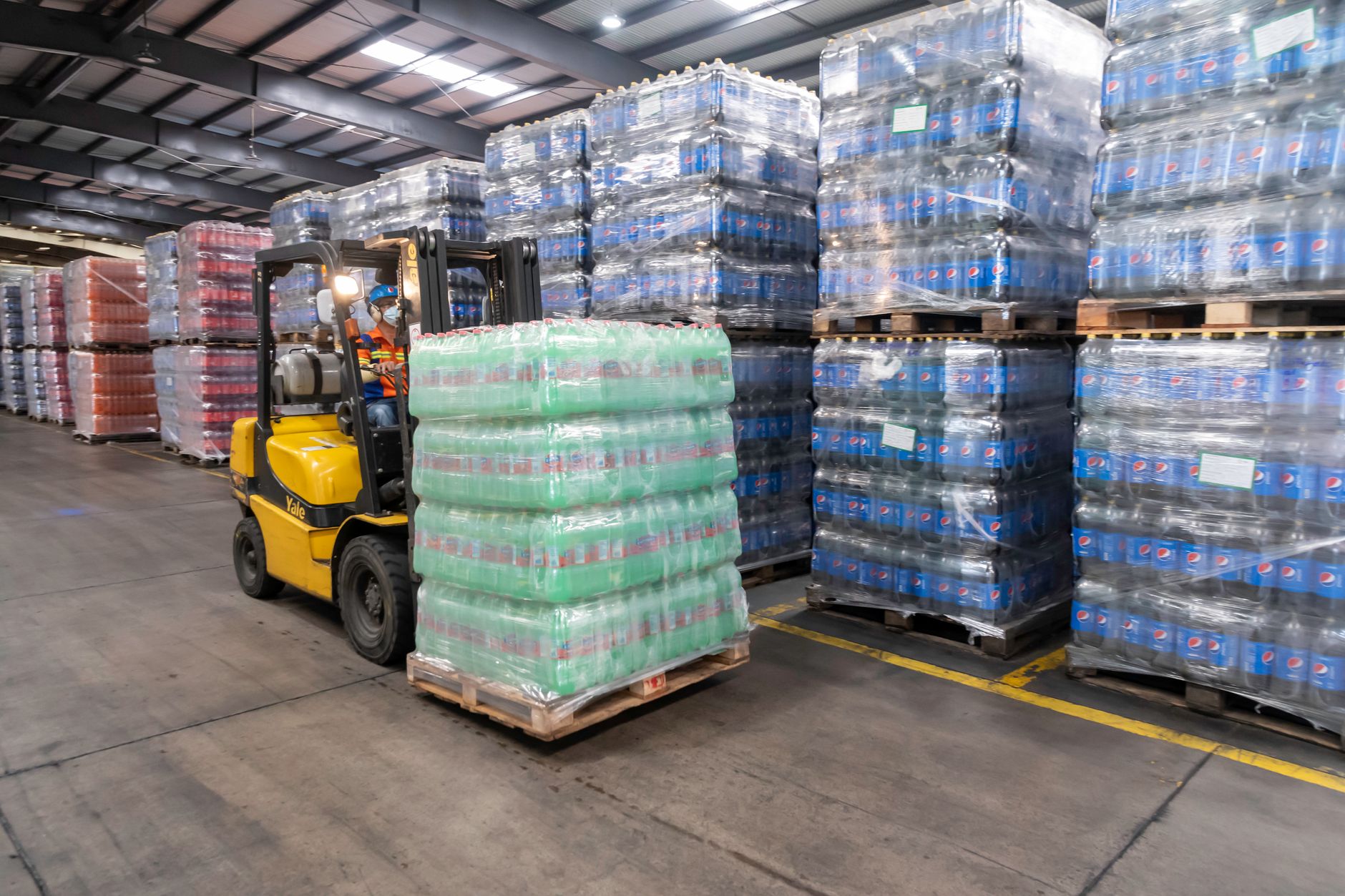 Stacks of bottled drinks on pallets in a stock area, representing the heavier summer replenishment cycles that reshape grocery backroom traffic.