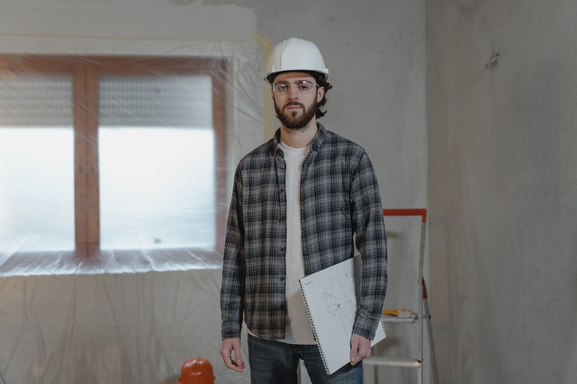 An engineer's desk with safety glasses lying on top of technical blueprints for a new facility layout, emphasizing the planning required by the 2026 A3 robot safety update.