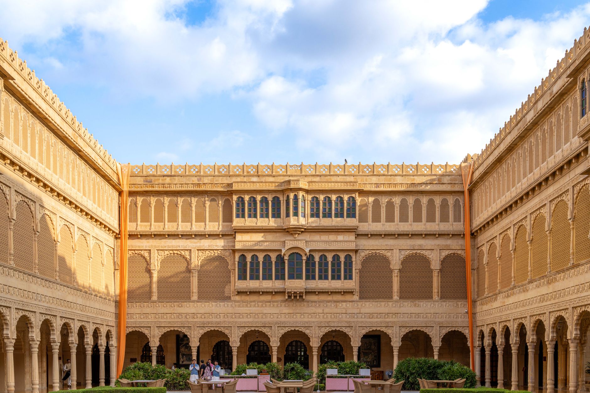 Strong sunlight falls across an exposed hotel courtyard where heat, glare, wind, and changing weather affect outdoor cleaning work.
