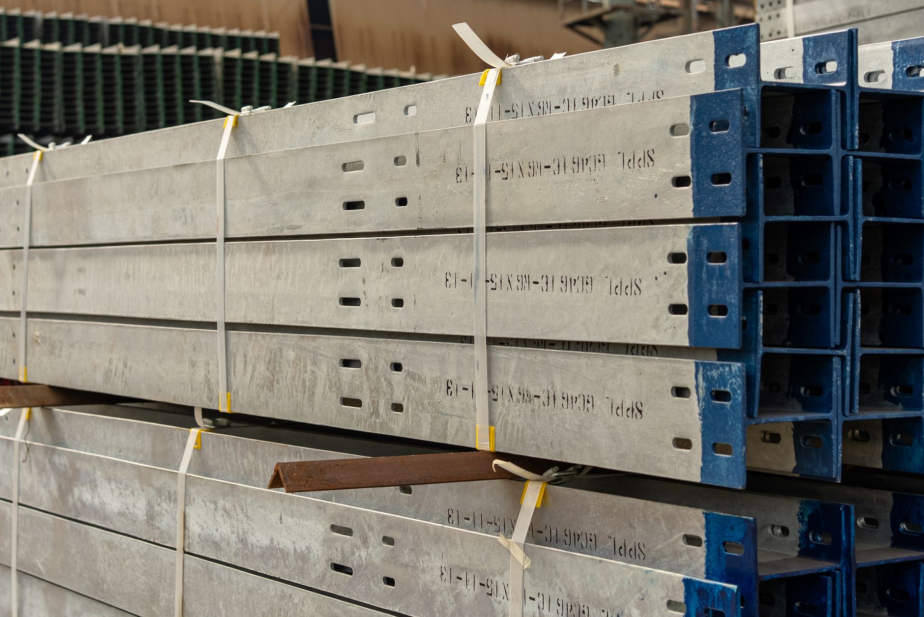 Stacks of structural steel components inside a large manufacturing warehouse, reflecting the plant-scale coordination behind Tate's multi-site welding network.
