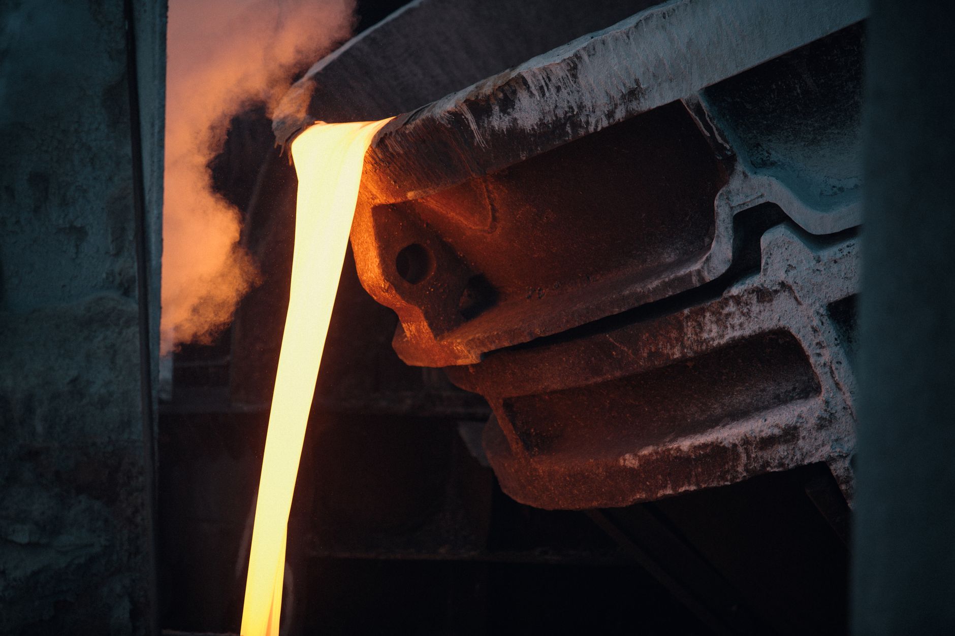Foundry worker near a glowing metal pour in a hot casting shop, illustrating the heat and handling conditions behind sand-core transfer work.