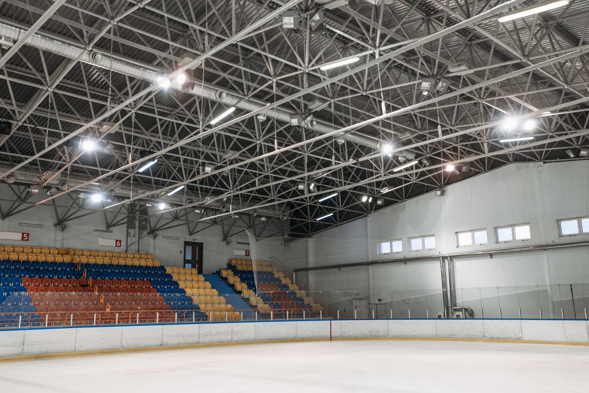 Overhead lighting and structure inside a large indoor arena, emphasizing the heavy energy loads carried above the fan experience.
