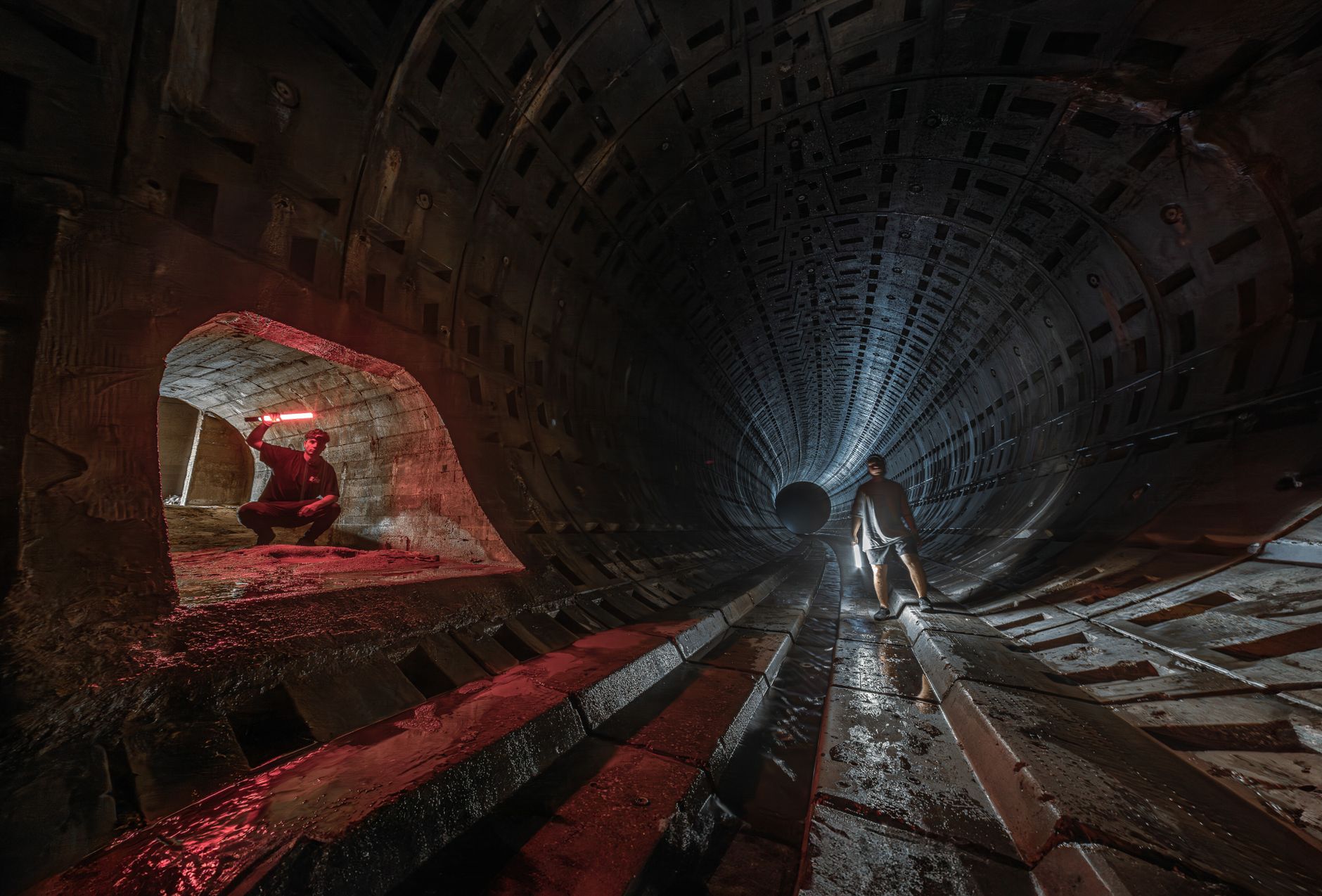 A worker examines the confined interior of an underground utility tunnel.