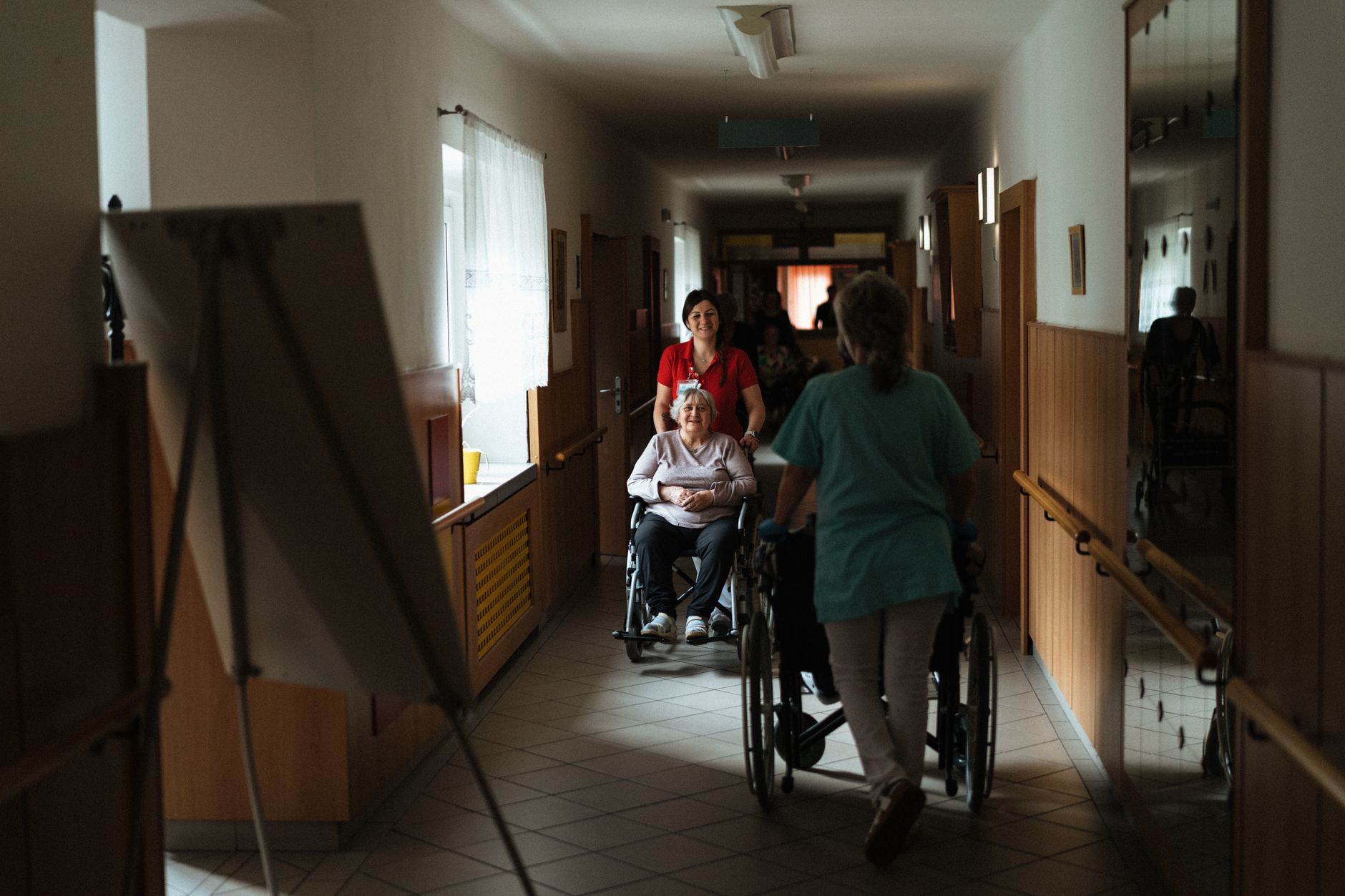 A quiet post-acute care hallway with mobility aids and patient rooms, setting the scene for repetitive transfer-heavy care work.